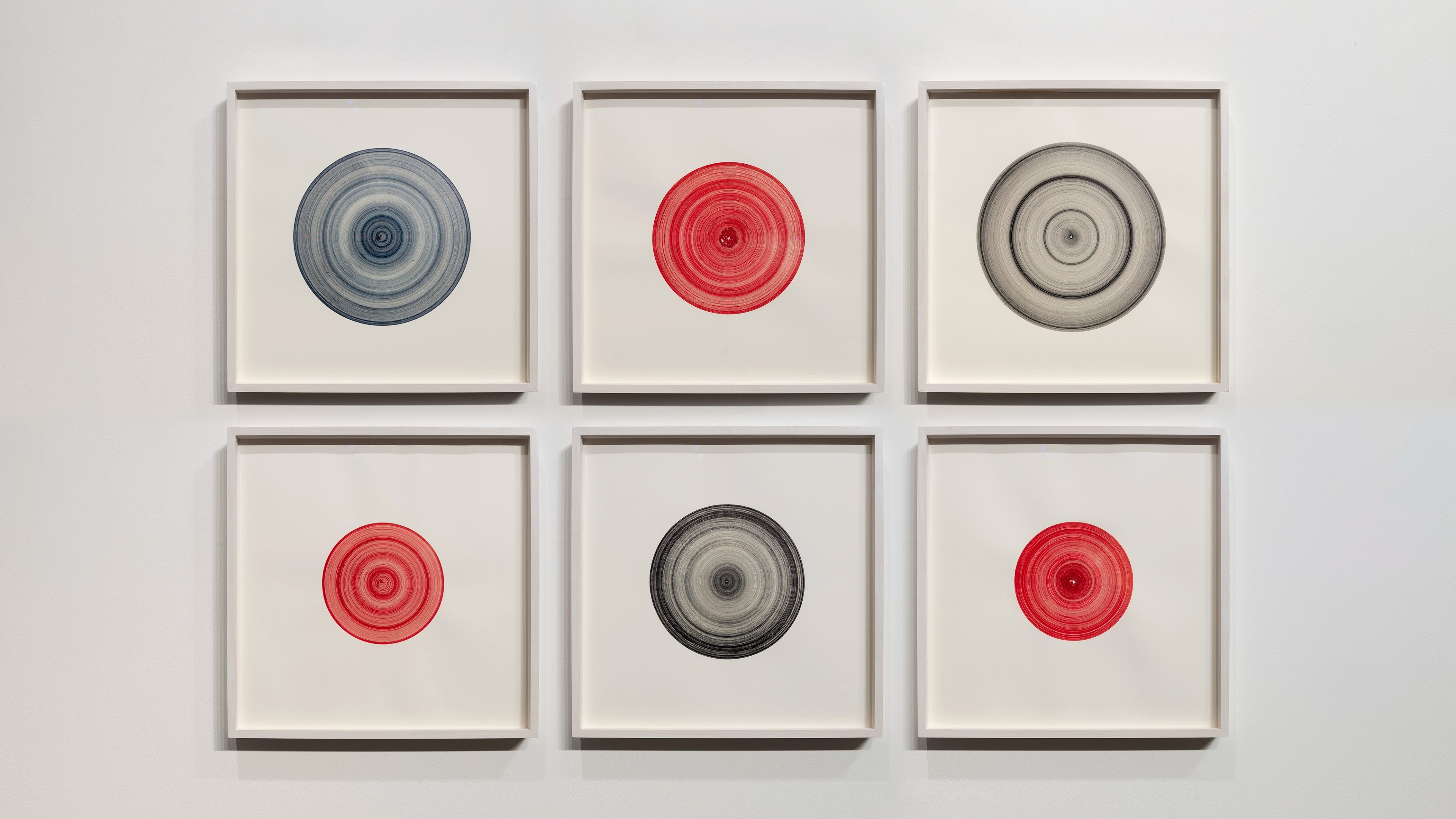 Six framed drawings arranged in two rows of three, each featuring concentric circles in blue, red, grey, and black on cream paper, mounted in grey frames
