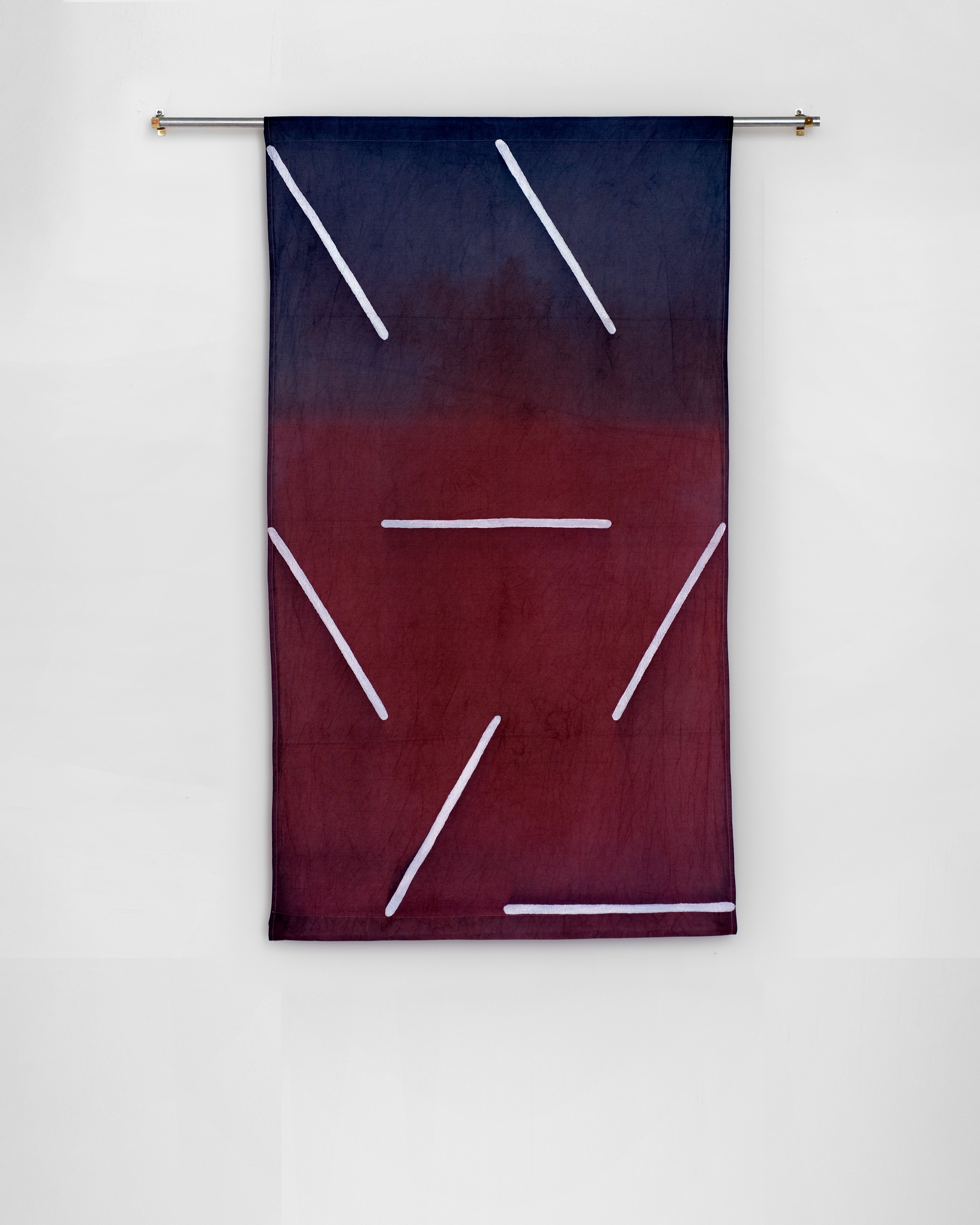 Hand-dyed cotton banner in deep navy and burgundy with white neon lines forming an abstracted face or mask-like composition hung from a brass rod