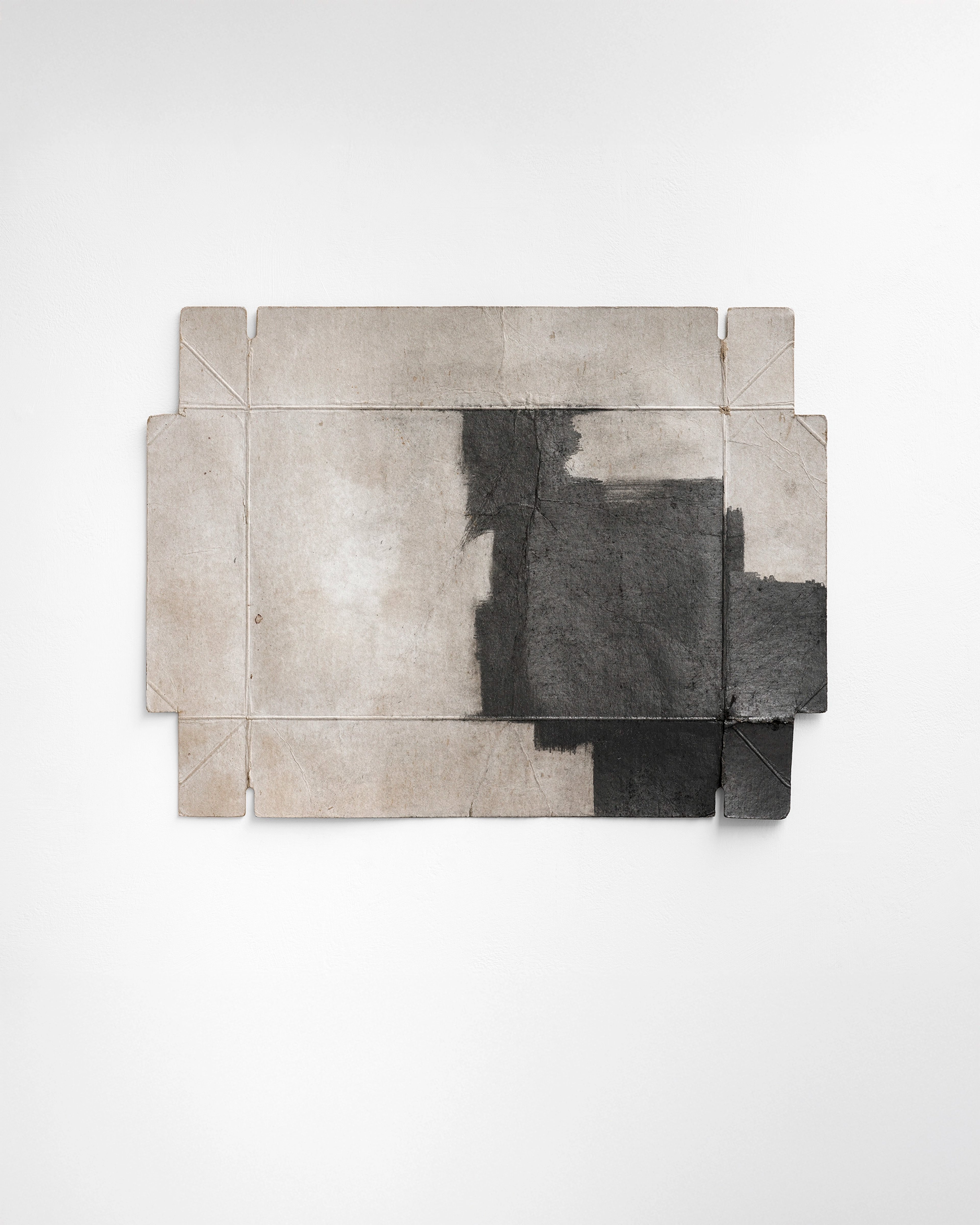 Graphite drawing on assembled cardboard panels with geometric cutouts, depicting dark architectural forms against light beige surfaces with visible seams and…