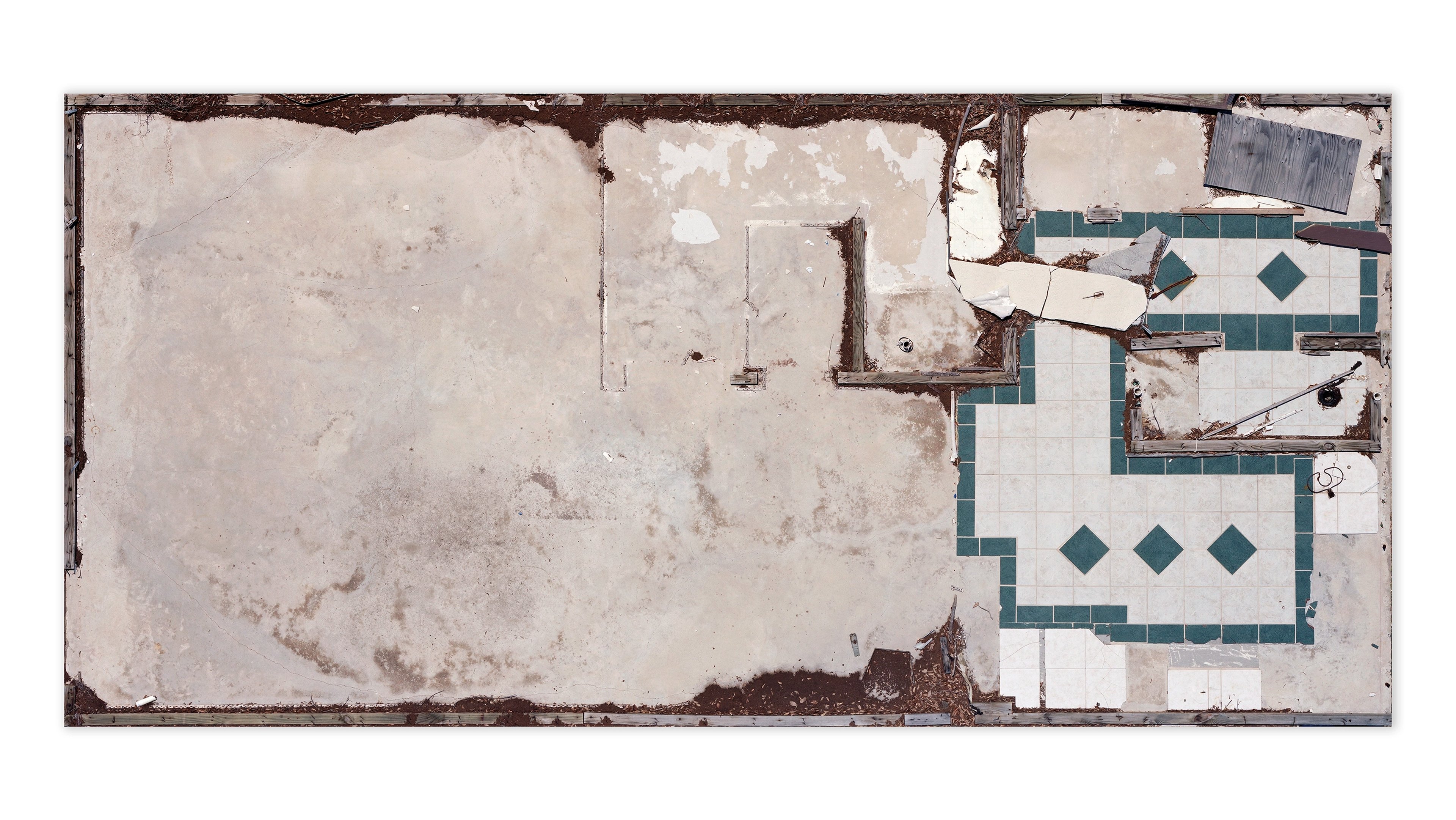 Aerial photograph of an abandoned residential interior with worn cream walls, visible doorways, and a tiled bathroom with teal and white diamond patterns
