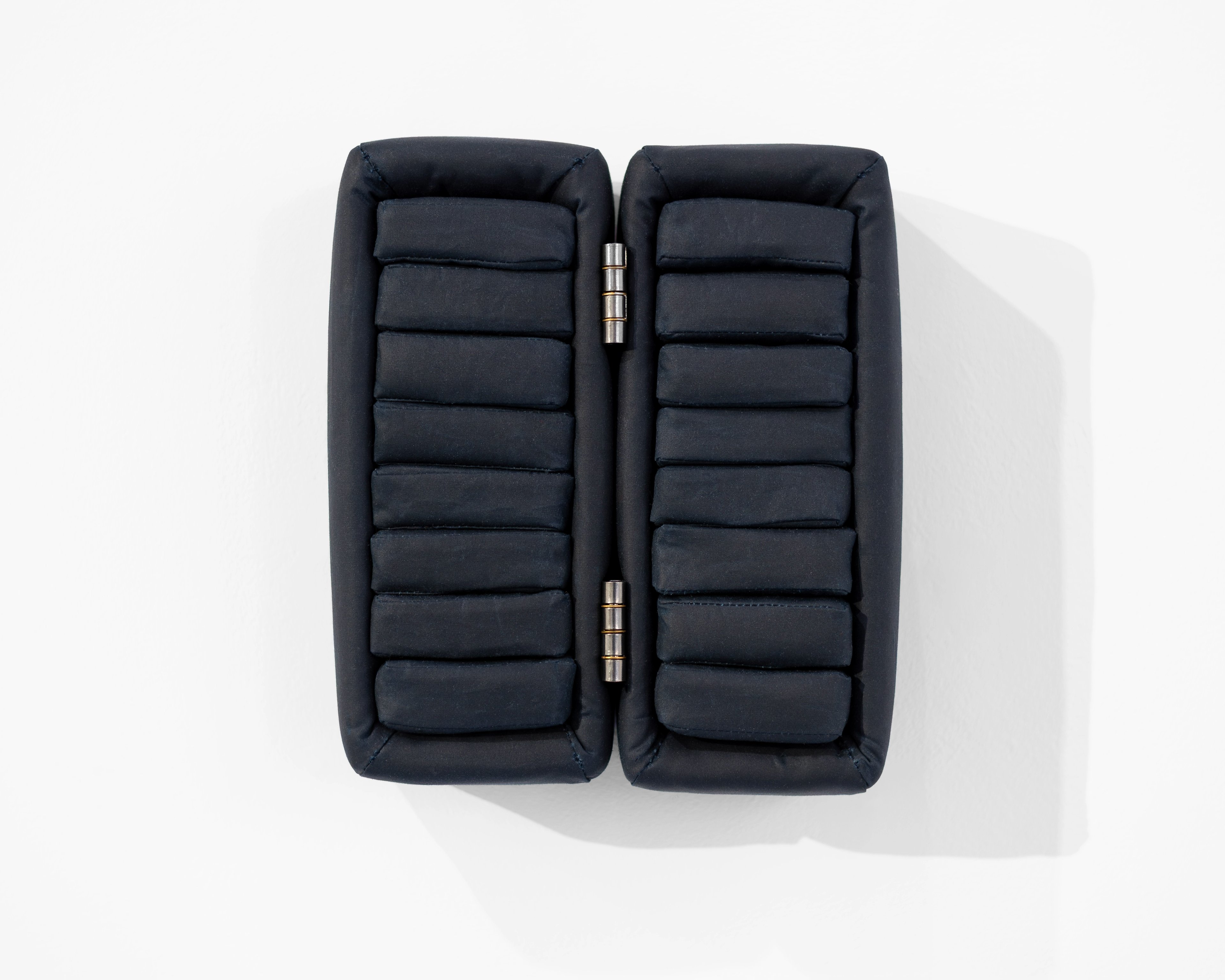 Two black quilted rectangular cushioned cases joined by metal hinges, viewed from above against a white background.