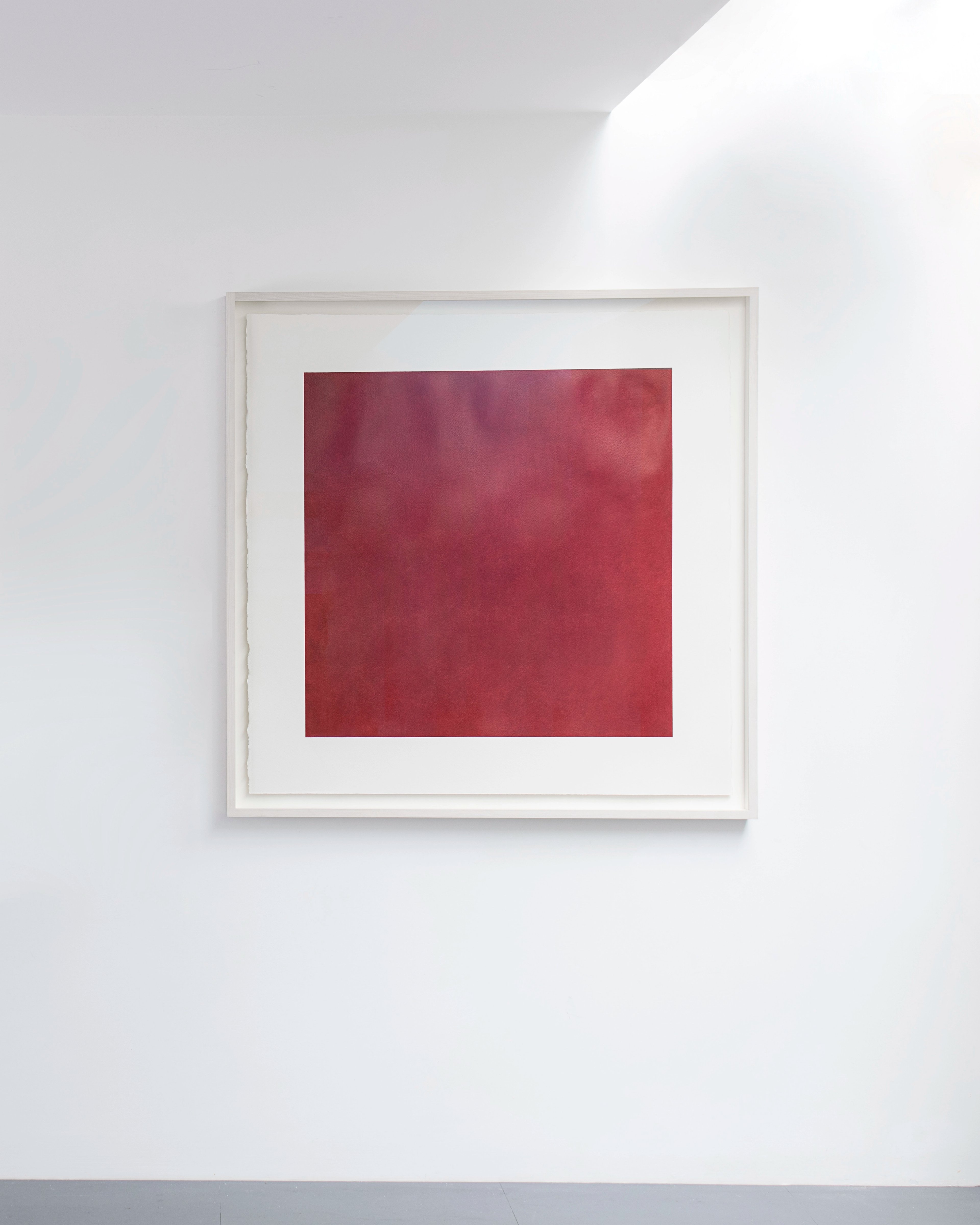 Framed drawing of a deep red square rendered in colored pencil, mounted on white board within a light wood frame hung on gallery wall
