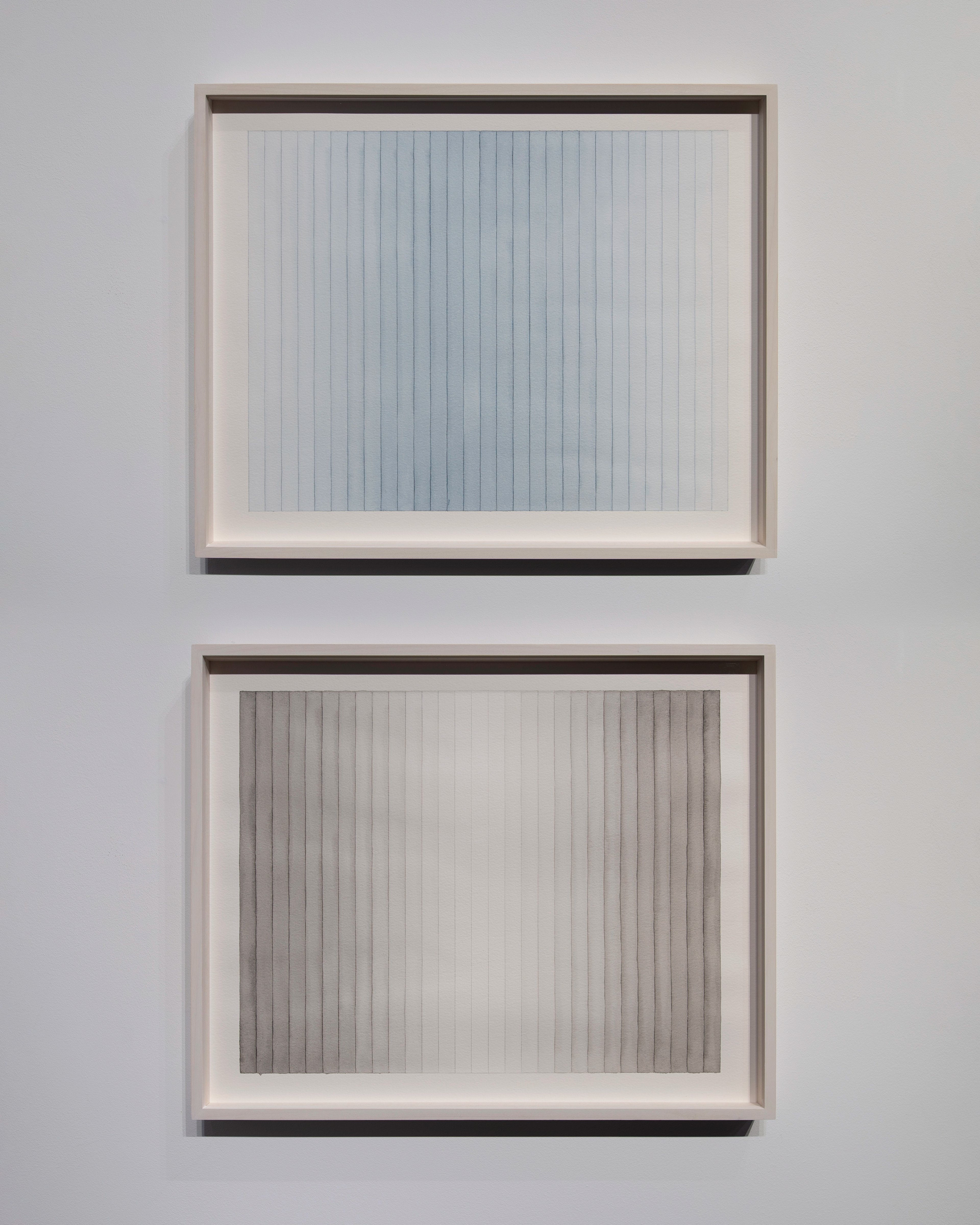 Two framed watercolour panels with vertical striations: upper work in pale blue-grey tones, lower in warm grey and cream, mounted in wooden frames with white…