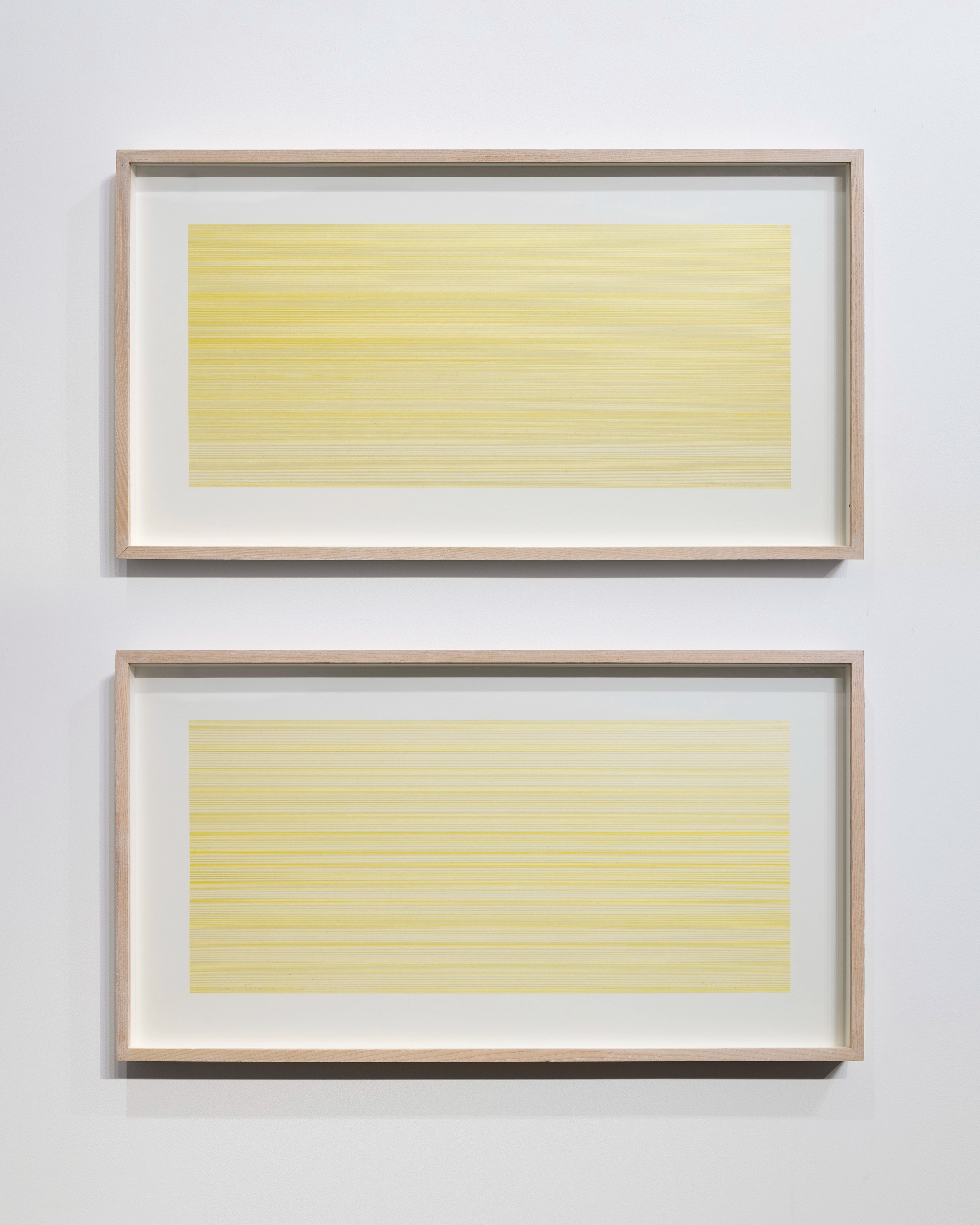 Two framed drawings stacked vertically, each with pale yellow horizontal lined patterns rendered in ink on mounted paper, set in natural wood frames against…