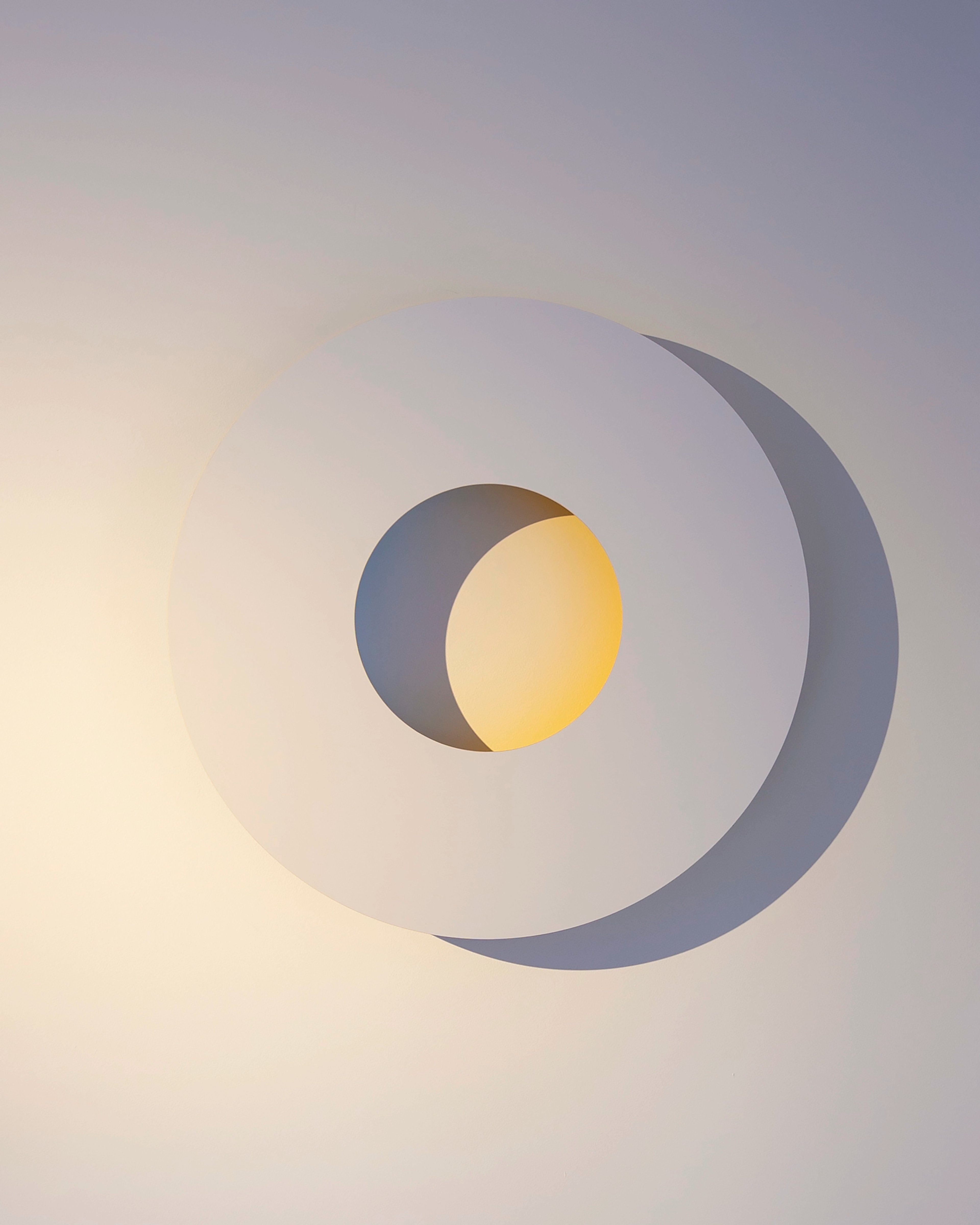 Concentric grey and lavender rings with a central yellow circle, painted on PVC and aluminium, creating a minimalist geometric composition against a soft gra…