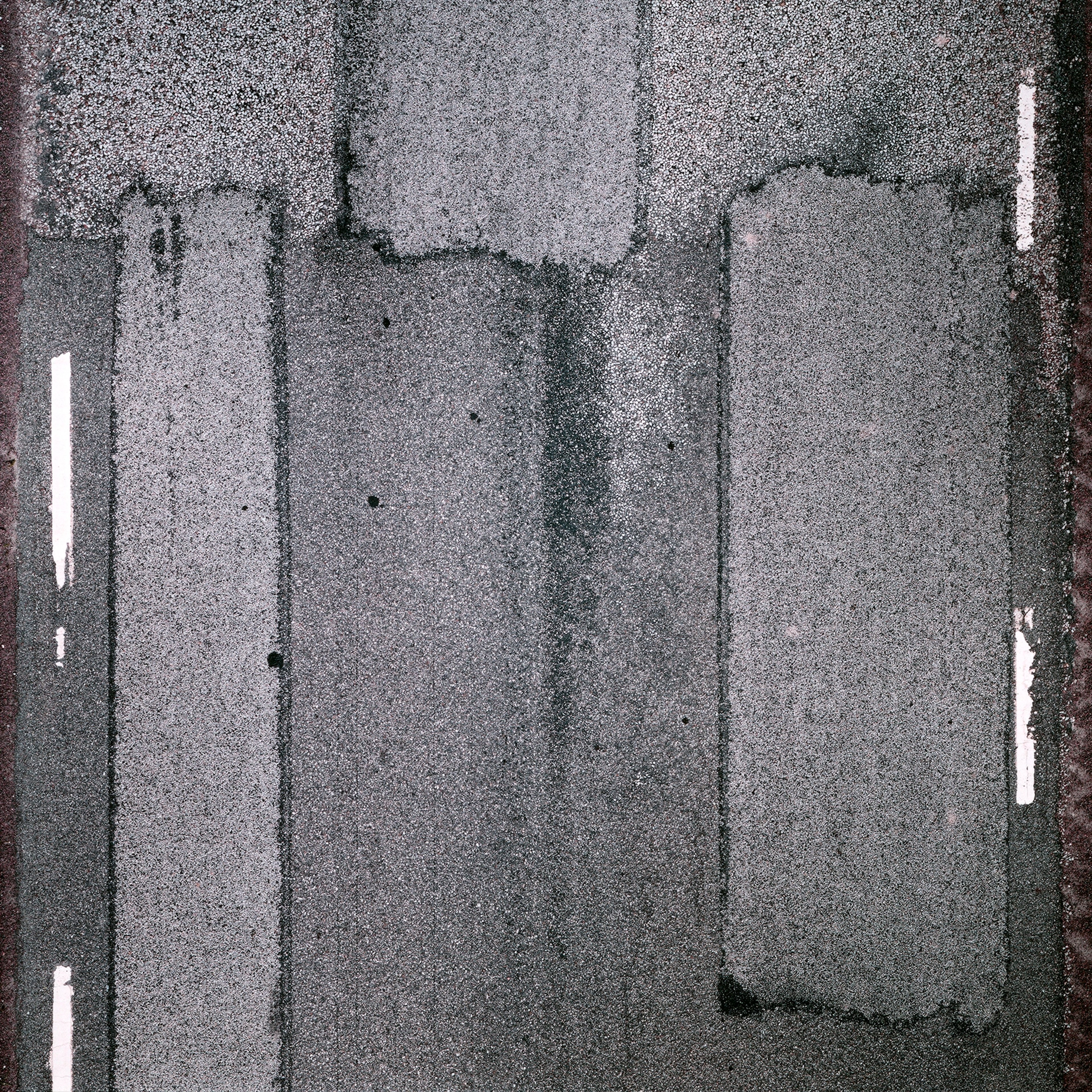 Overhead view of asphalt road surface with white lane markings, subtle terrain variations, and grainy photographic texture in grey tones