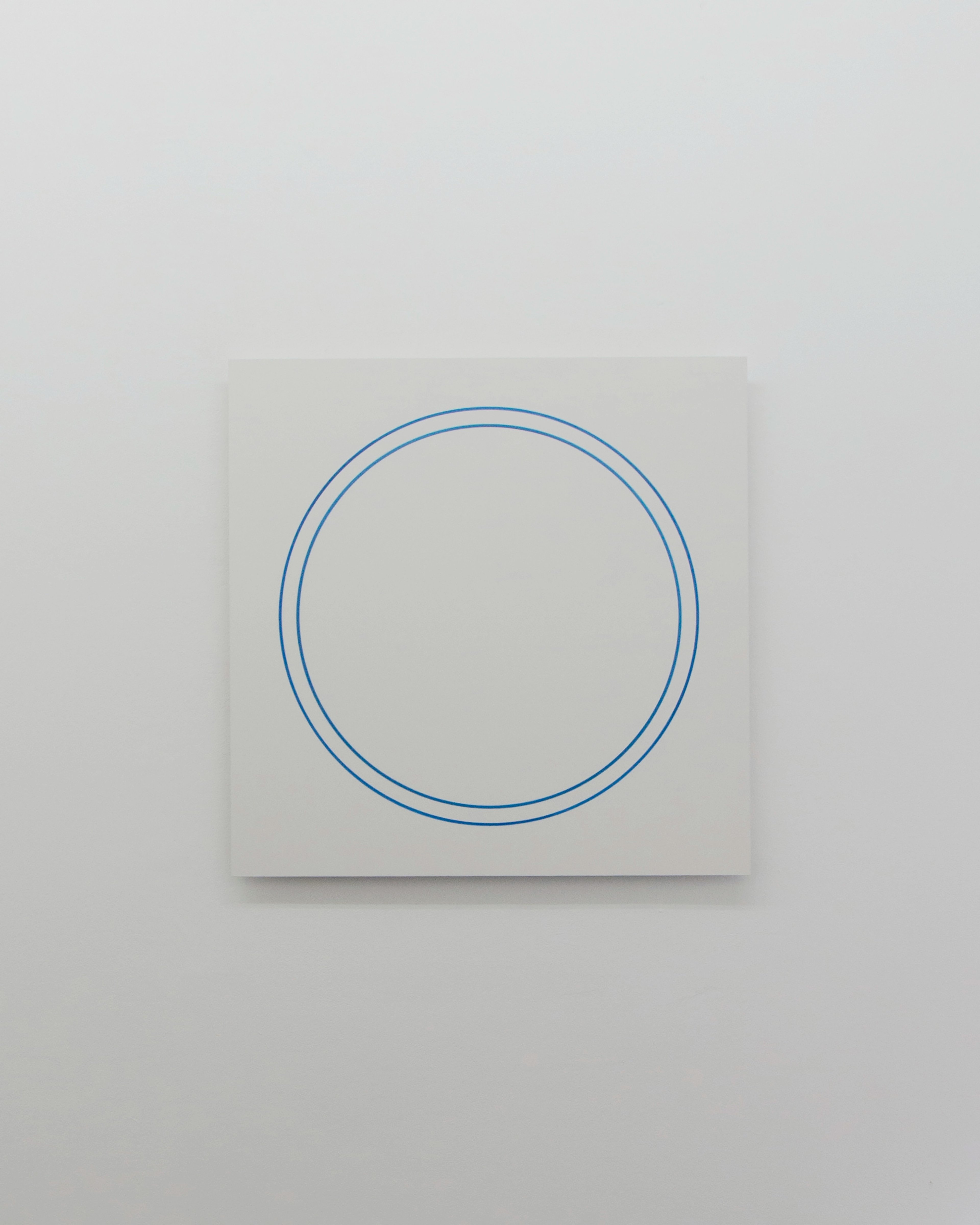 Blue concentric circles drawn in thin lines on a white square panel mounted on a grey wall