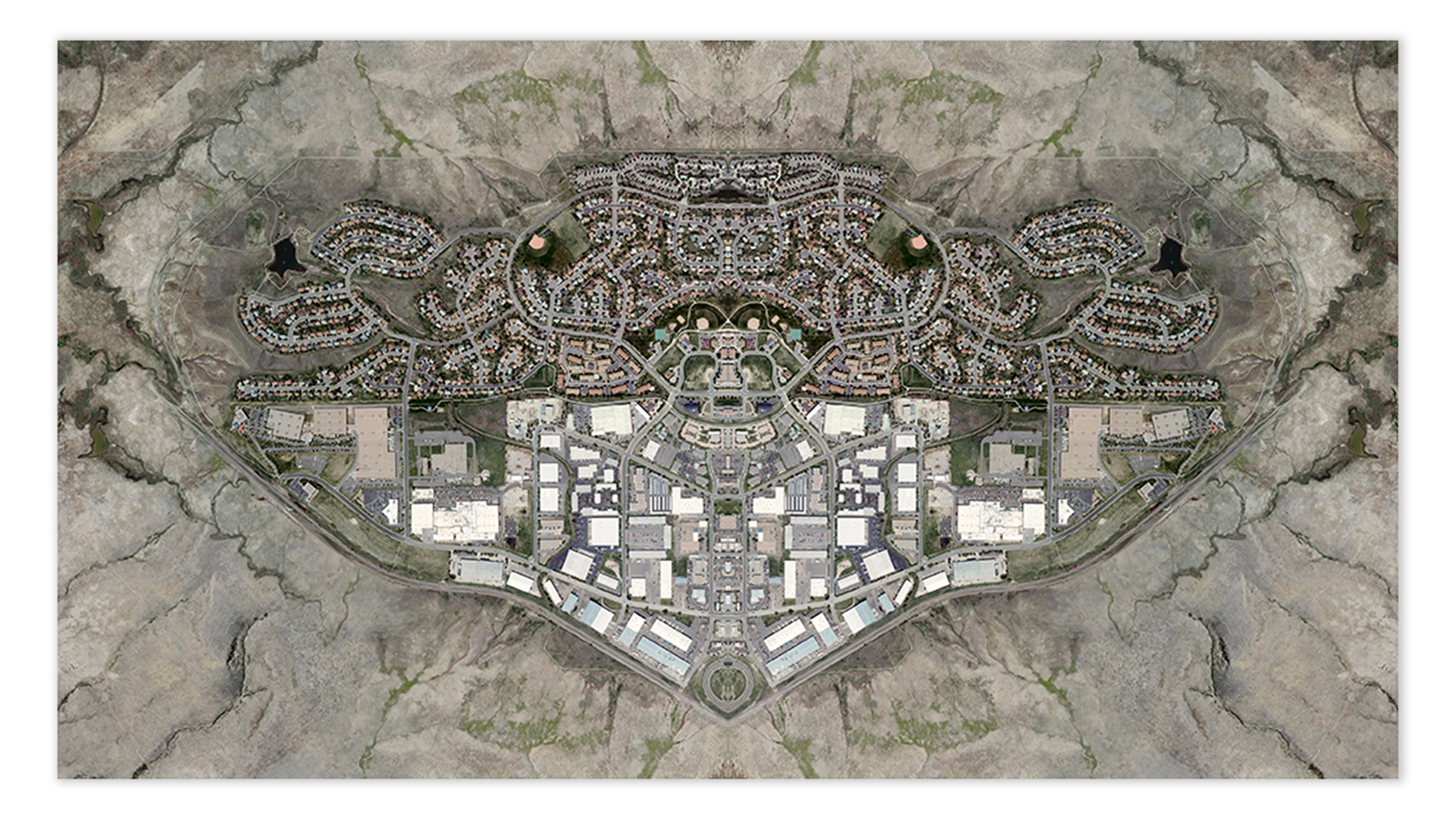 Aerial plan of a sprawling symmetrical development with dense residential neighborhoods flanking a central institutional complex, set within barren desert la…