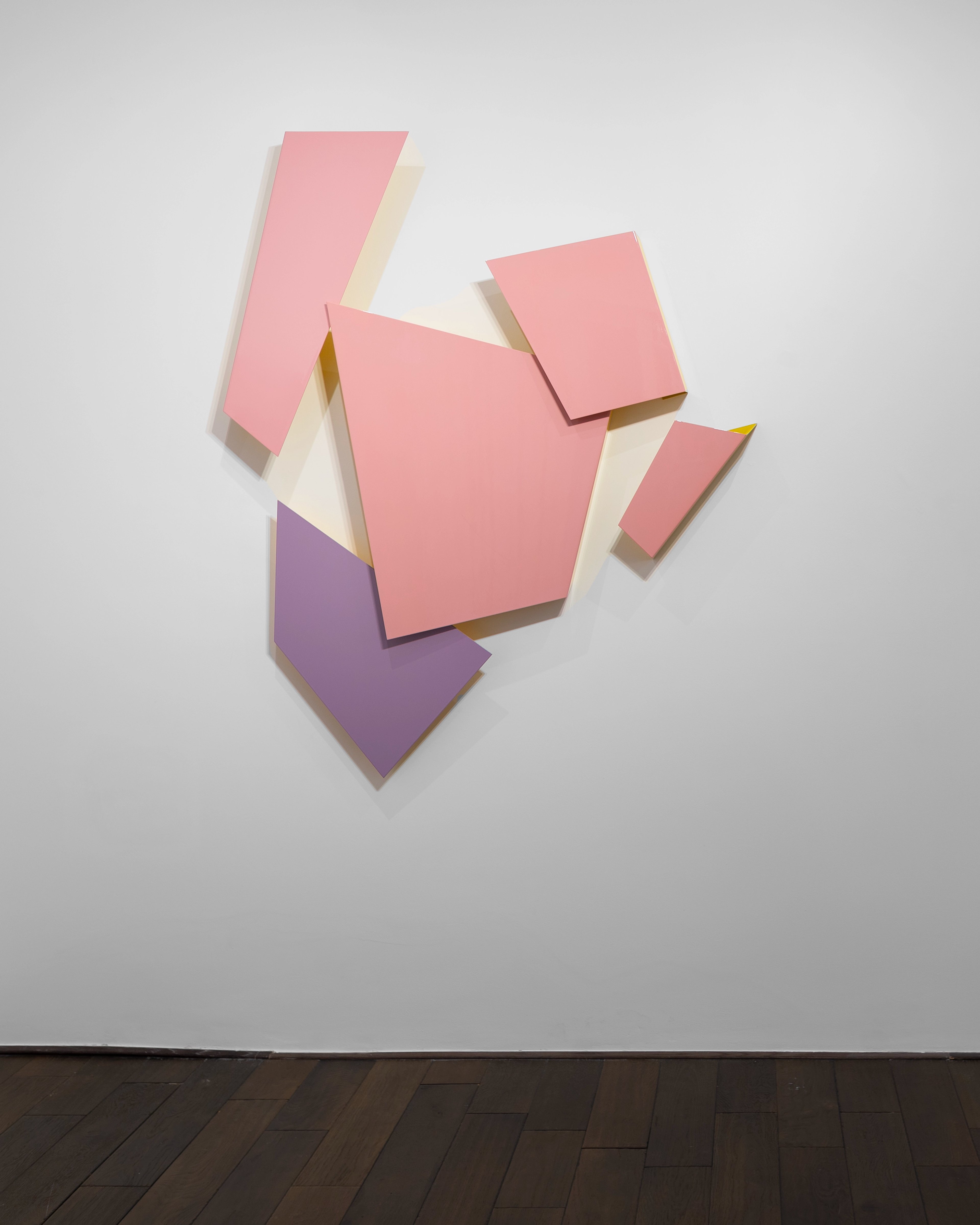 Interlocking geometric shapes in pink, purple, and cream lacquer on aluminium, mounted on a white wall with cast shadows
