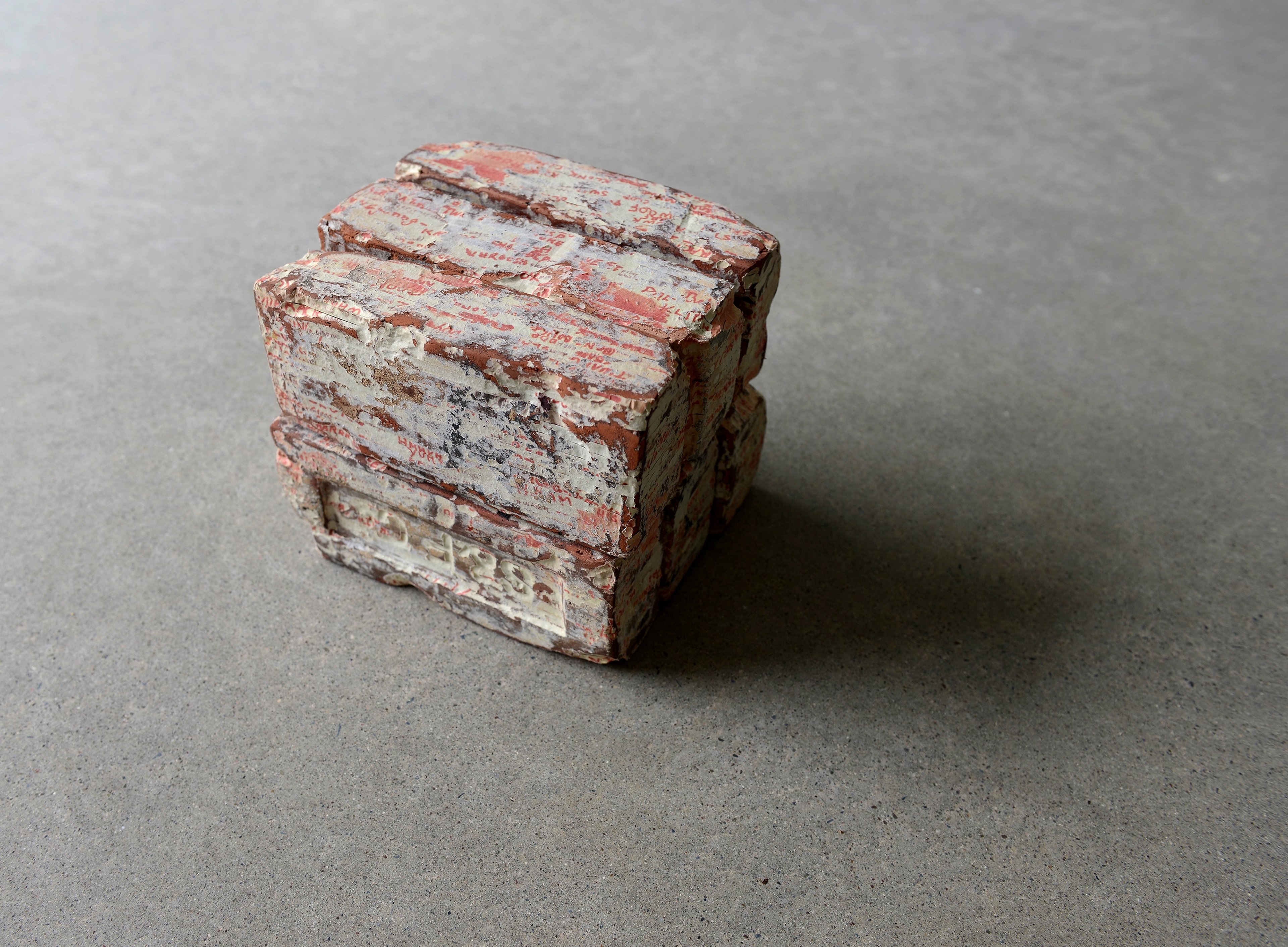 Stacked vintage clay brick fragment with weathered red and white surface, cut paper artwork displayed on neutral ground