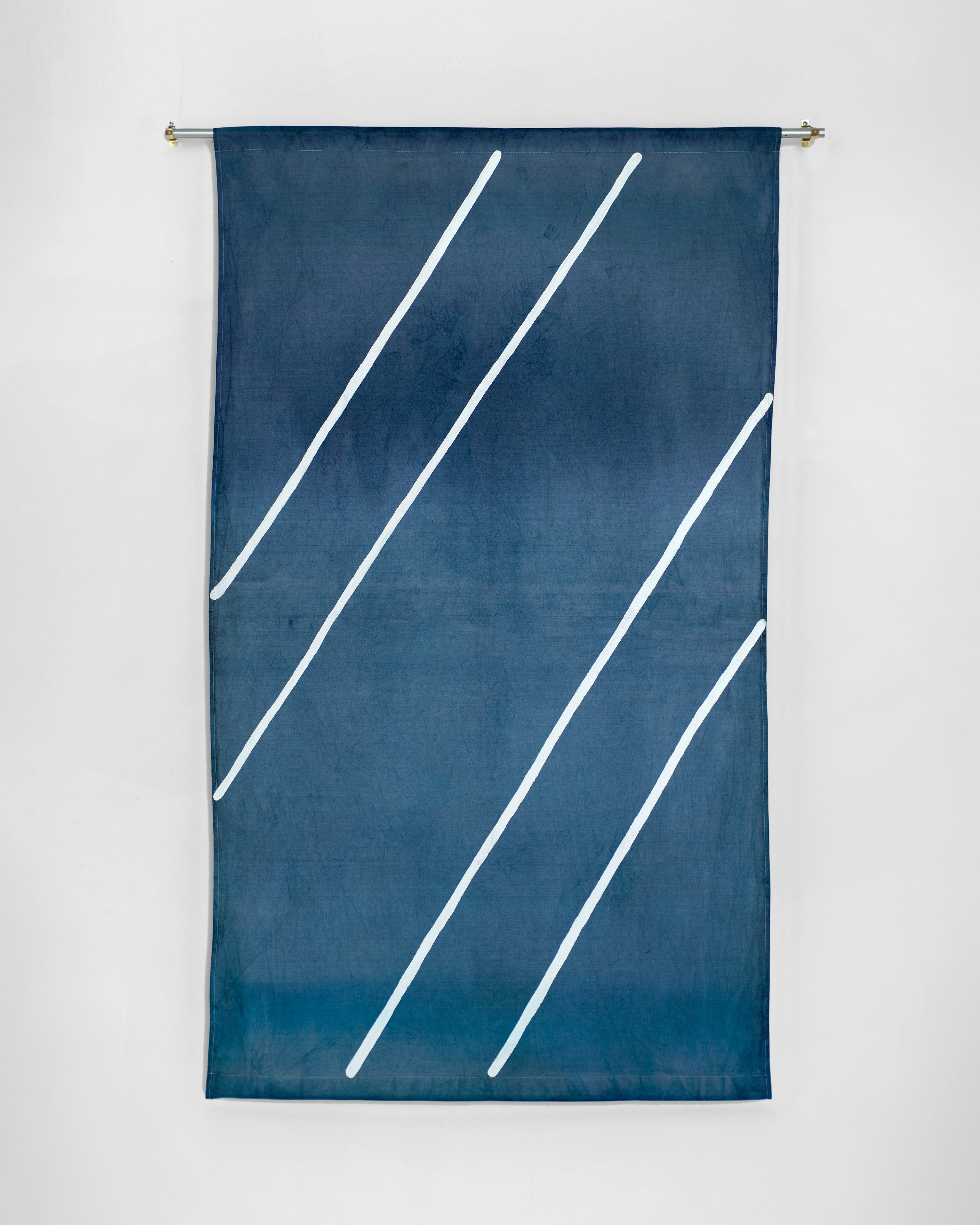 Hand-dyed dark blue cotton fabric with five white diagonal lines in acrylic paint, hung on a rod against white gallery wall