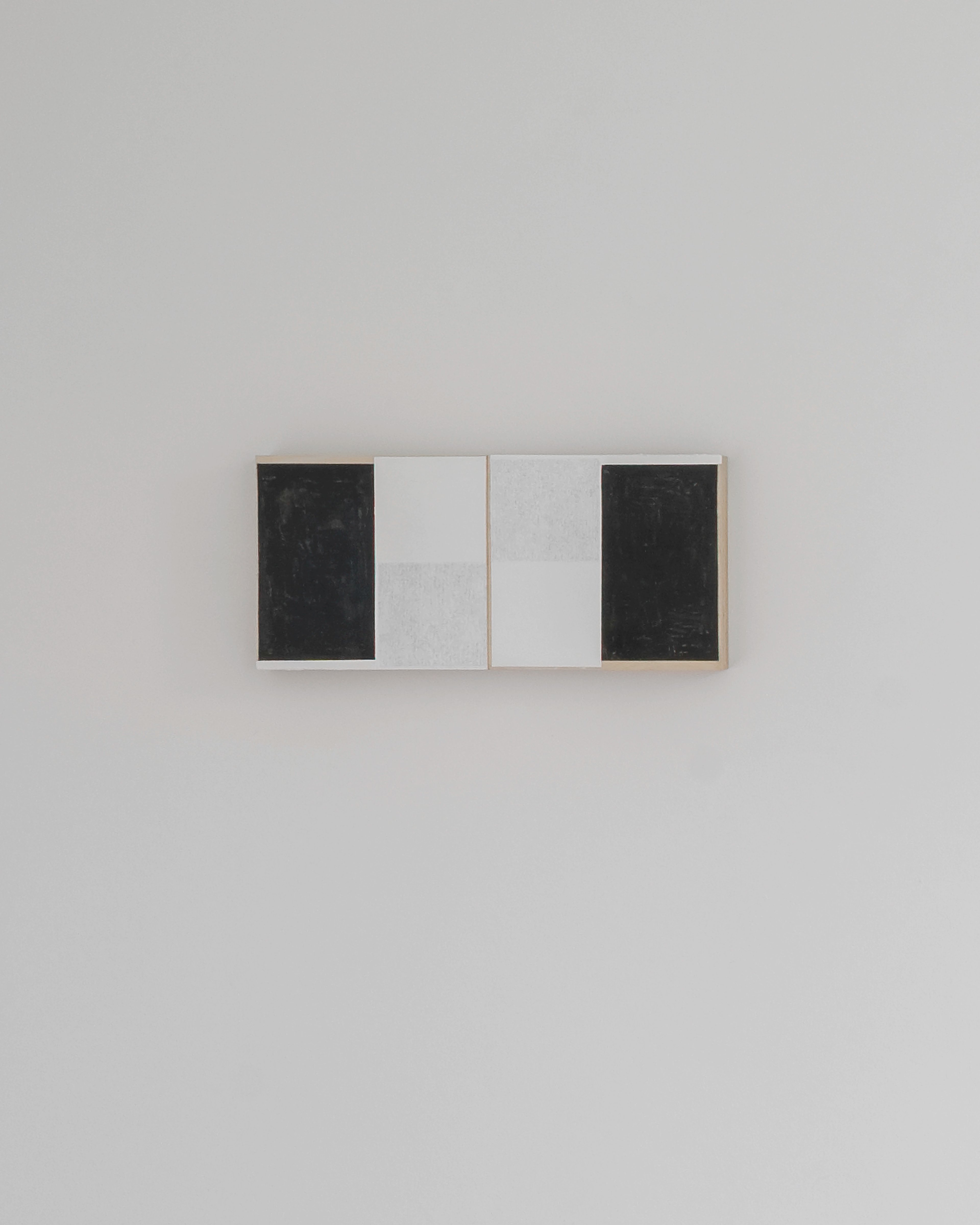 Four rectangular panels in light wood frame alternating between black charcoal surfaces and white painted areas, arranged horizontally on a neutral wall