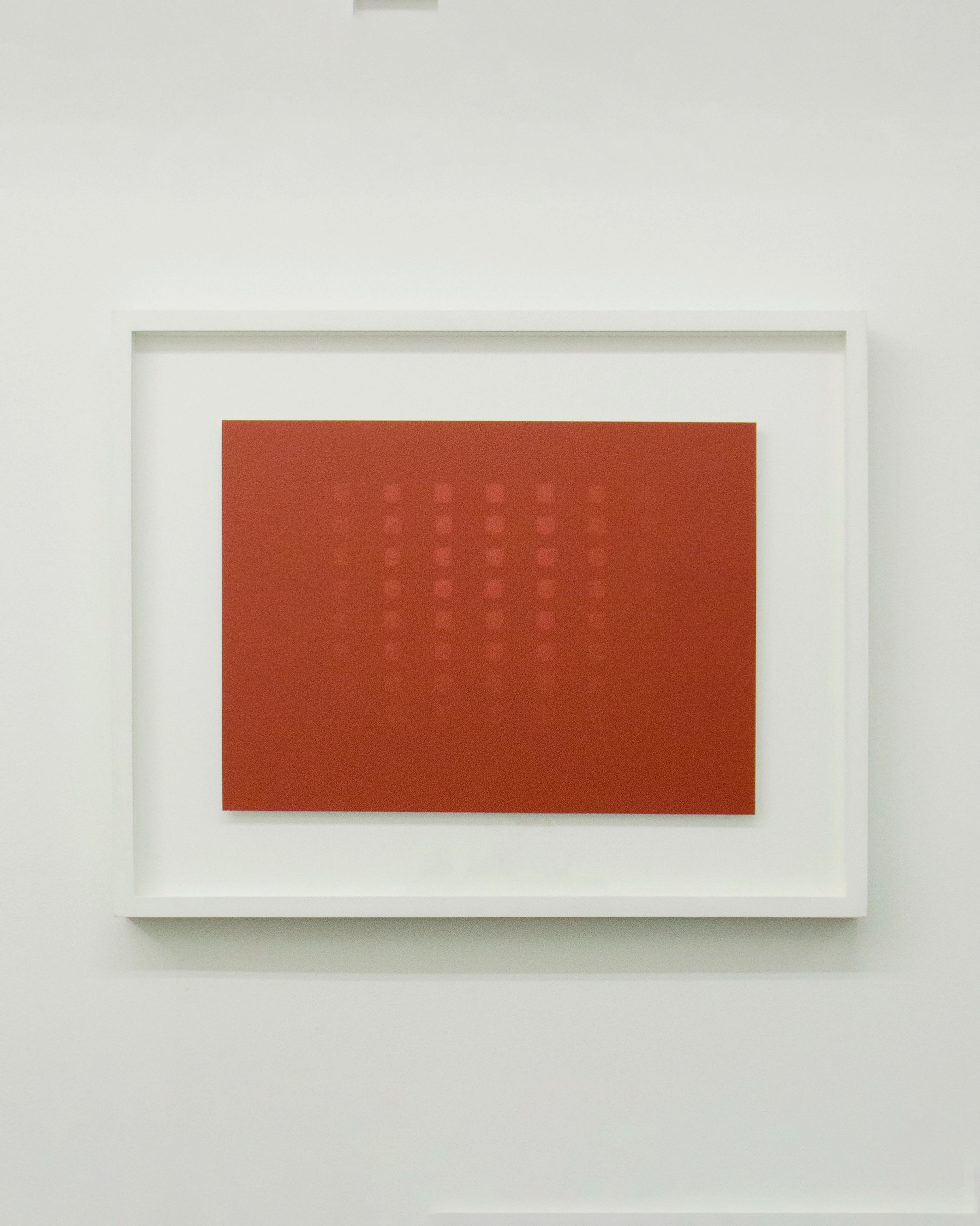 Rust-red rectangular wax transfer on white-framed Dibond panel, with faint embossed grid pattern suggesting Japanese text characters across its surface