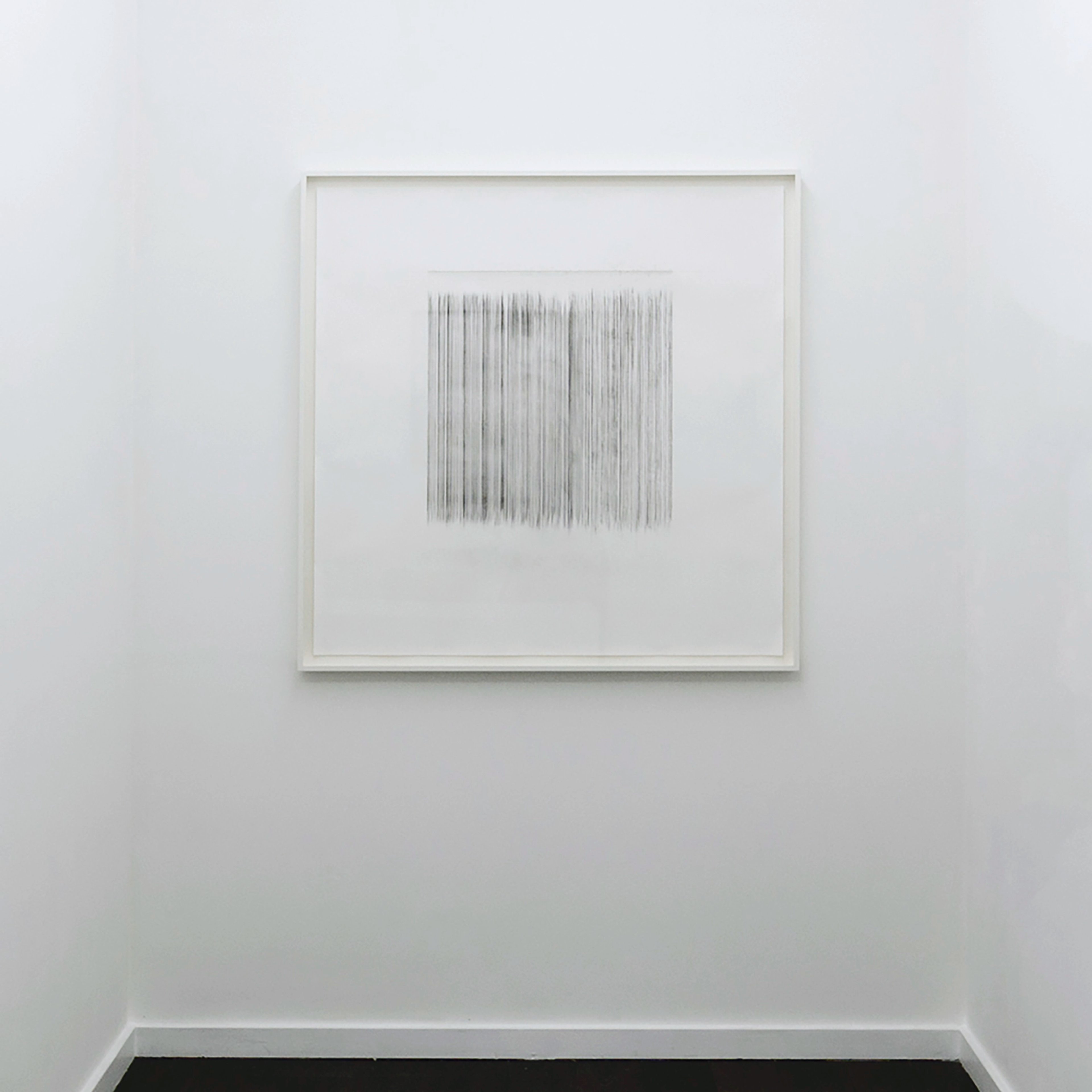 Fine linear graphite marks form a dense vertical striped rectangle on white paper in a white frame, suggesting measured or plumbed lines.