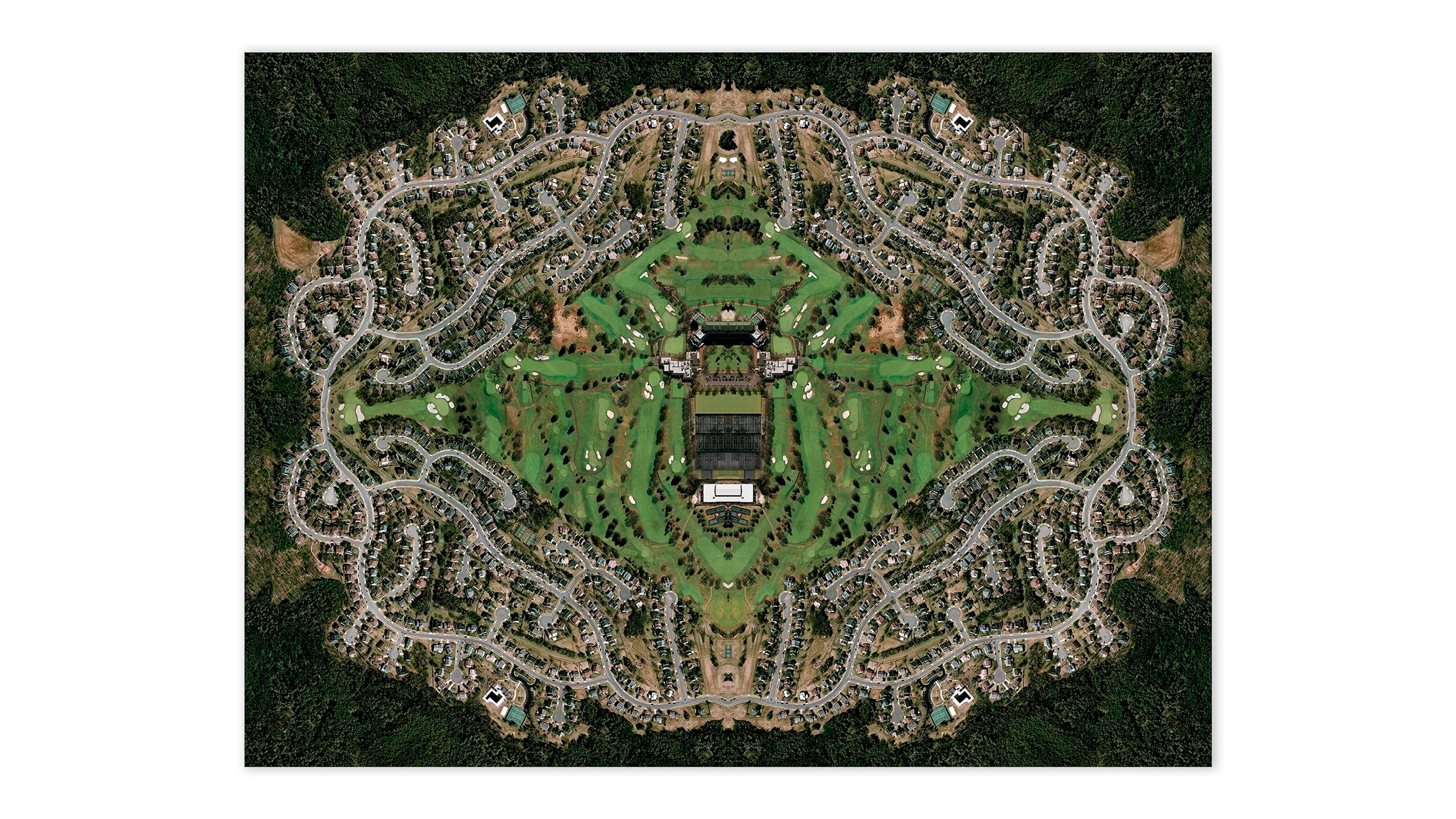 Aerial photograph of a suburban housing development with symmetrical curved streets and dense tree cover, creating a kaleidoscopic pattern around a central g…