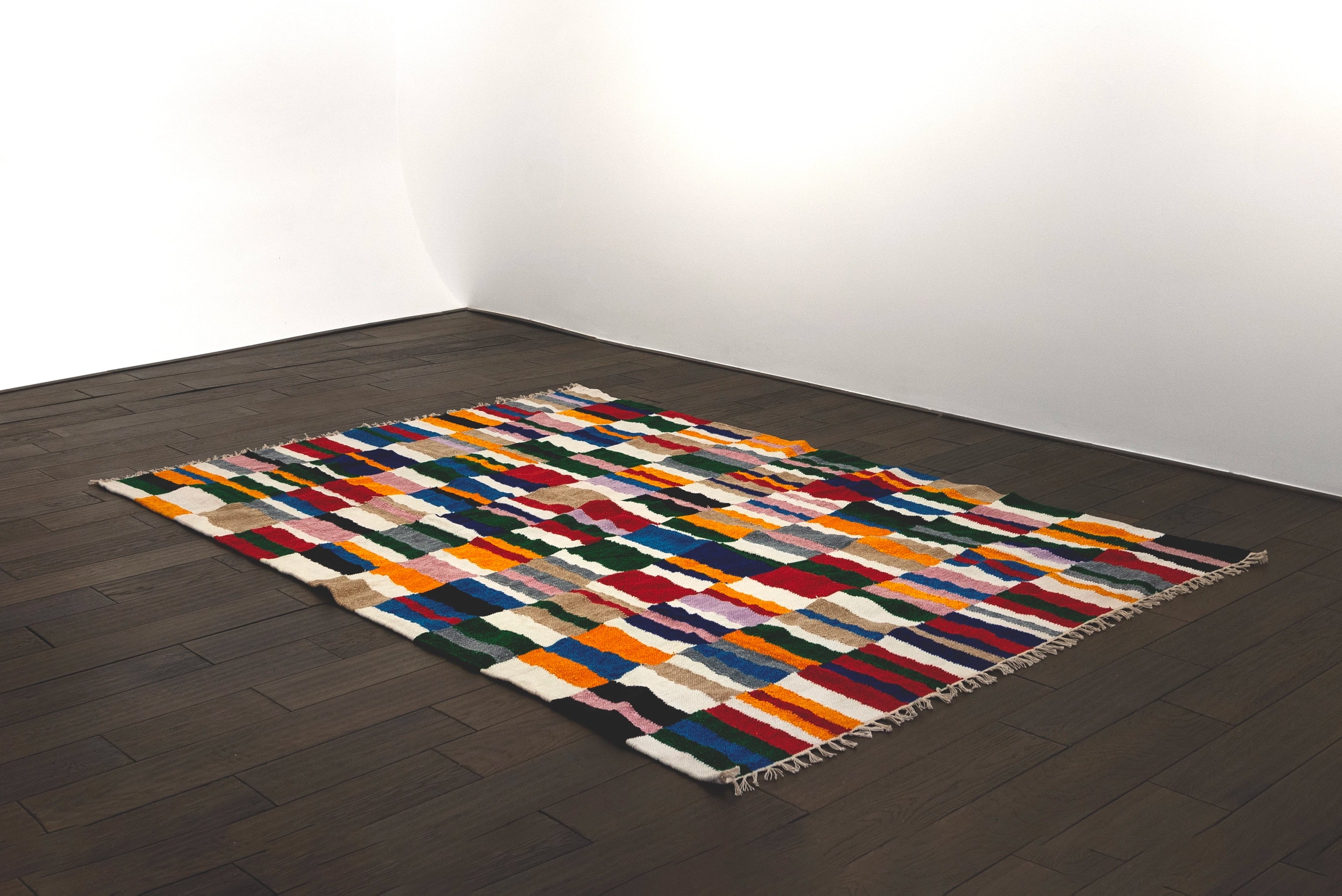 Handwoven velvet rug with horizontal stripes of vibrant colors including blue, orange, red, yellow, and cream arranged in a rhythmic pattern on dark wooden f…