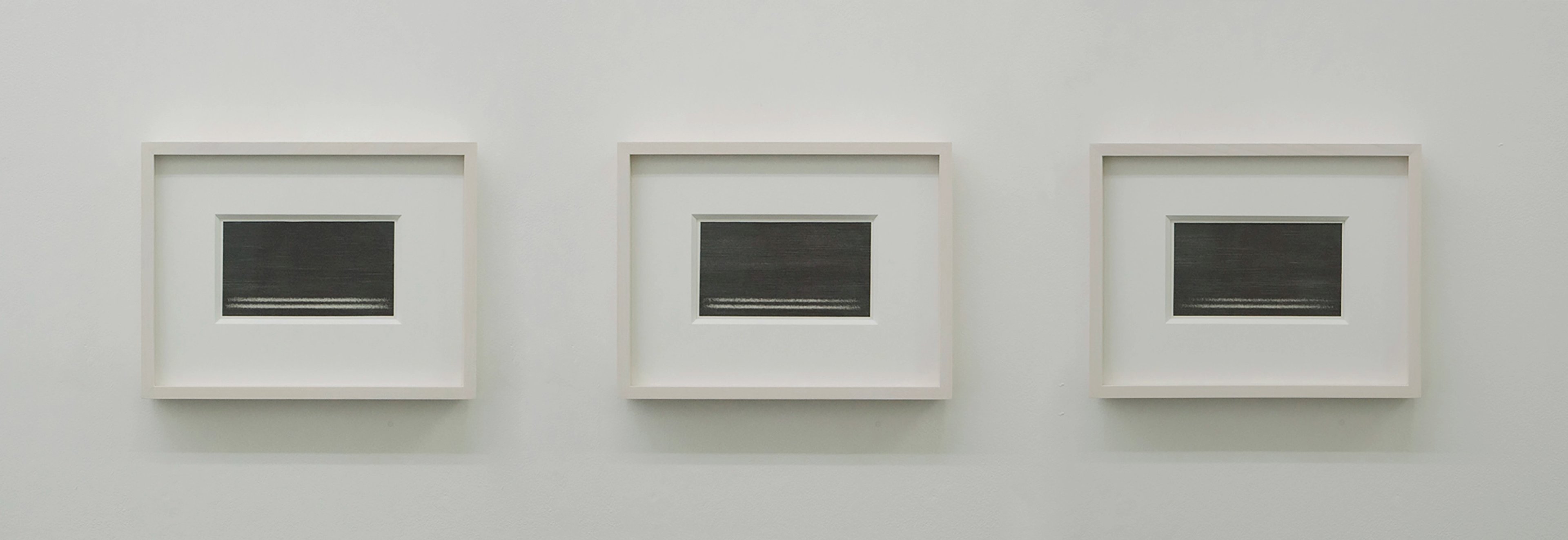 Three framed graphite transfer pieces mounted on rag paper, each featuring horizontal linear marks within dark rectangular forms, arranged in a horizontal tr…