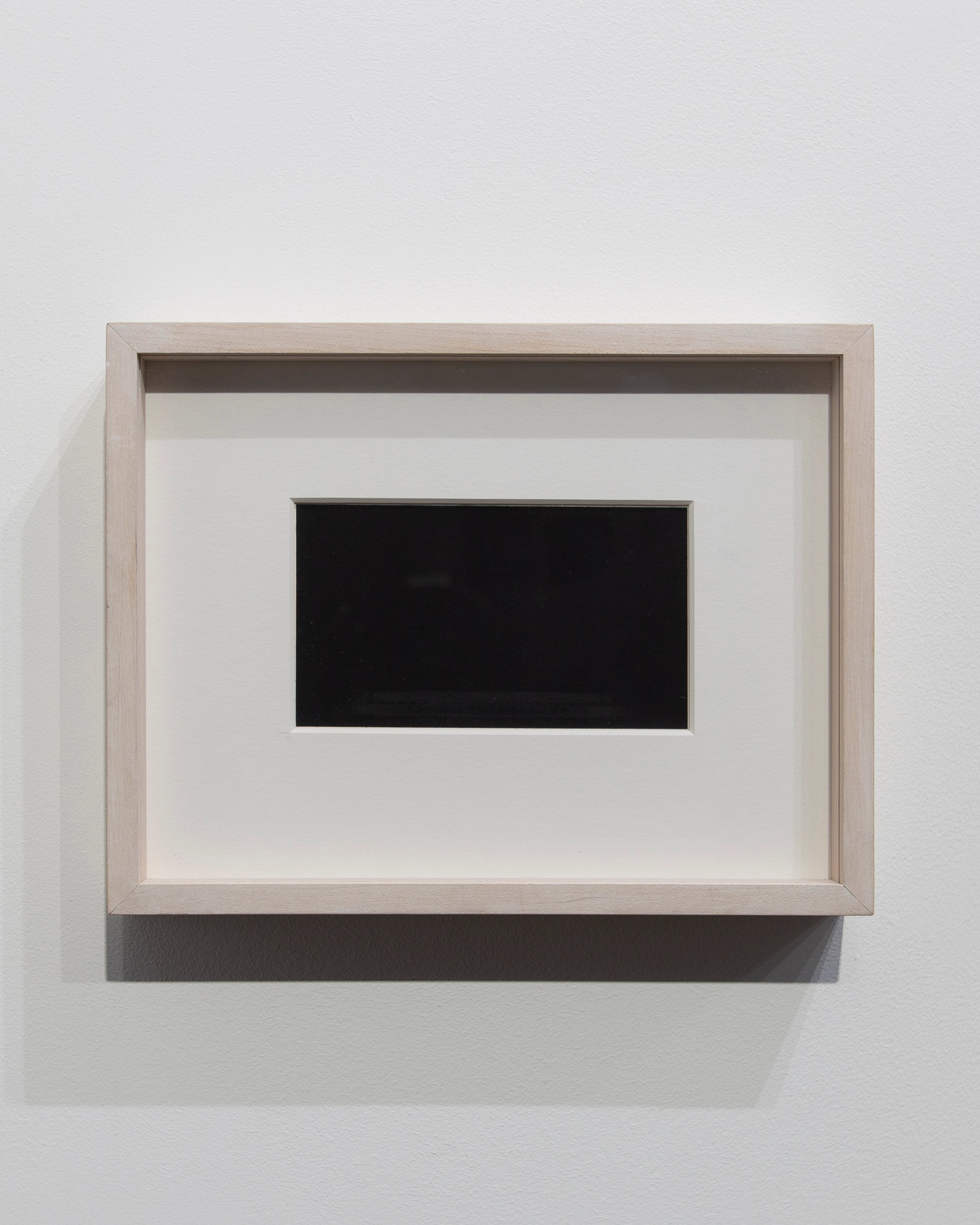 Framed wax transfer on rag paper mounted horizontally, displaying a single black rectangular form centered on cream-colored background, set within natural wo…