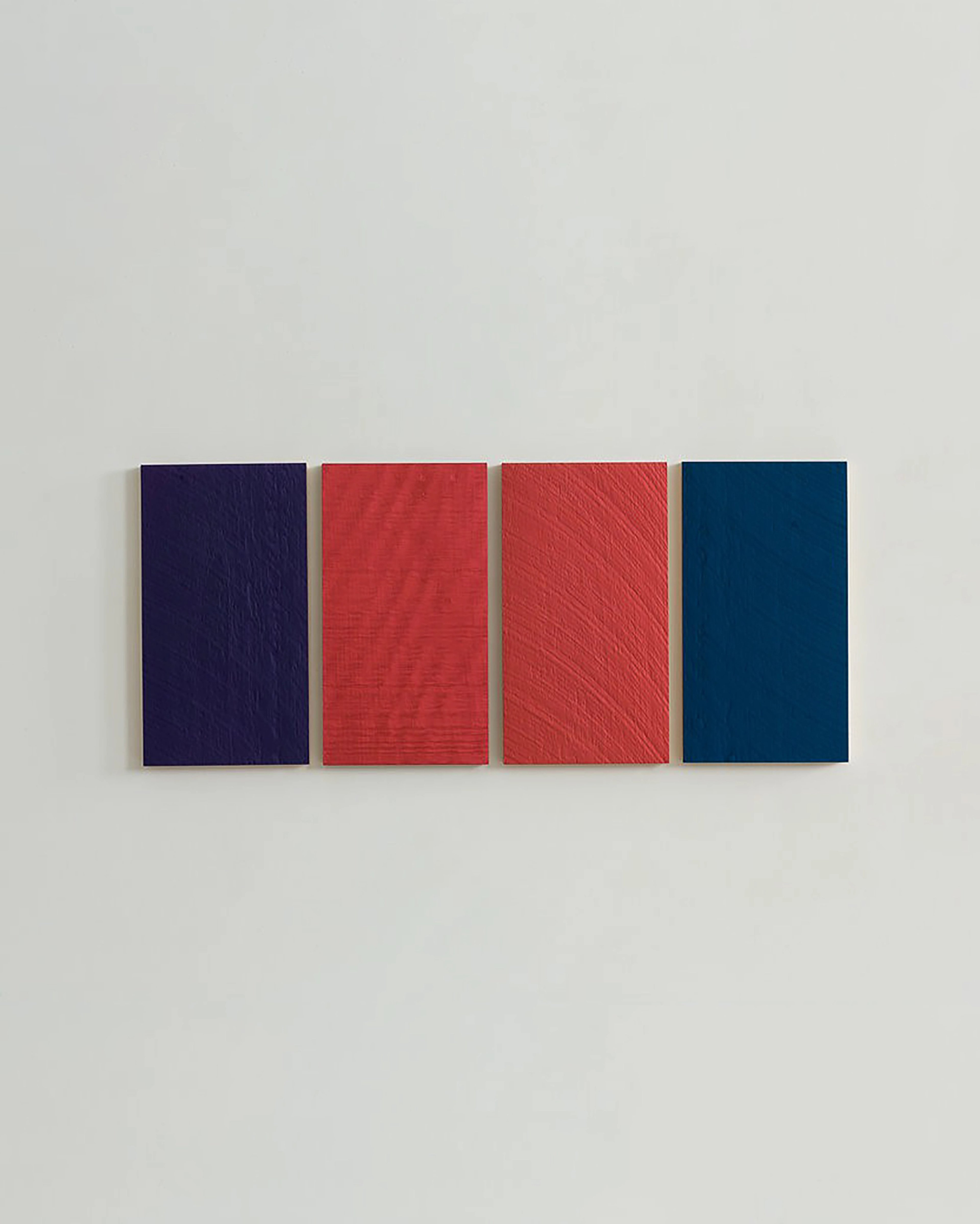 Four vertical wooden panels with textured surfaces in deep navy, bright red, coral red with diagonal lines, and dark teal, arranged in a row on a white wall