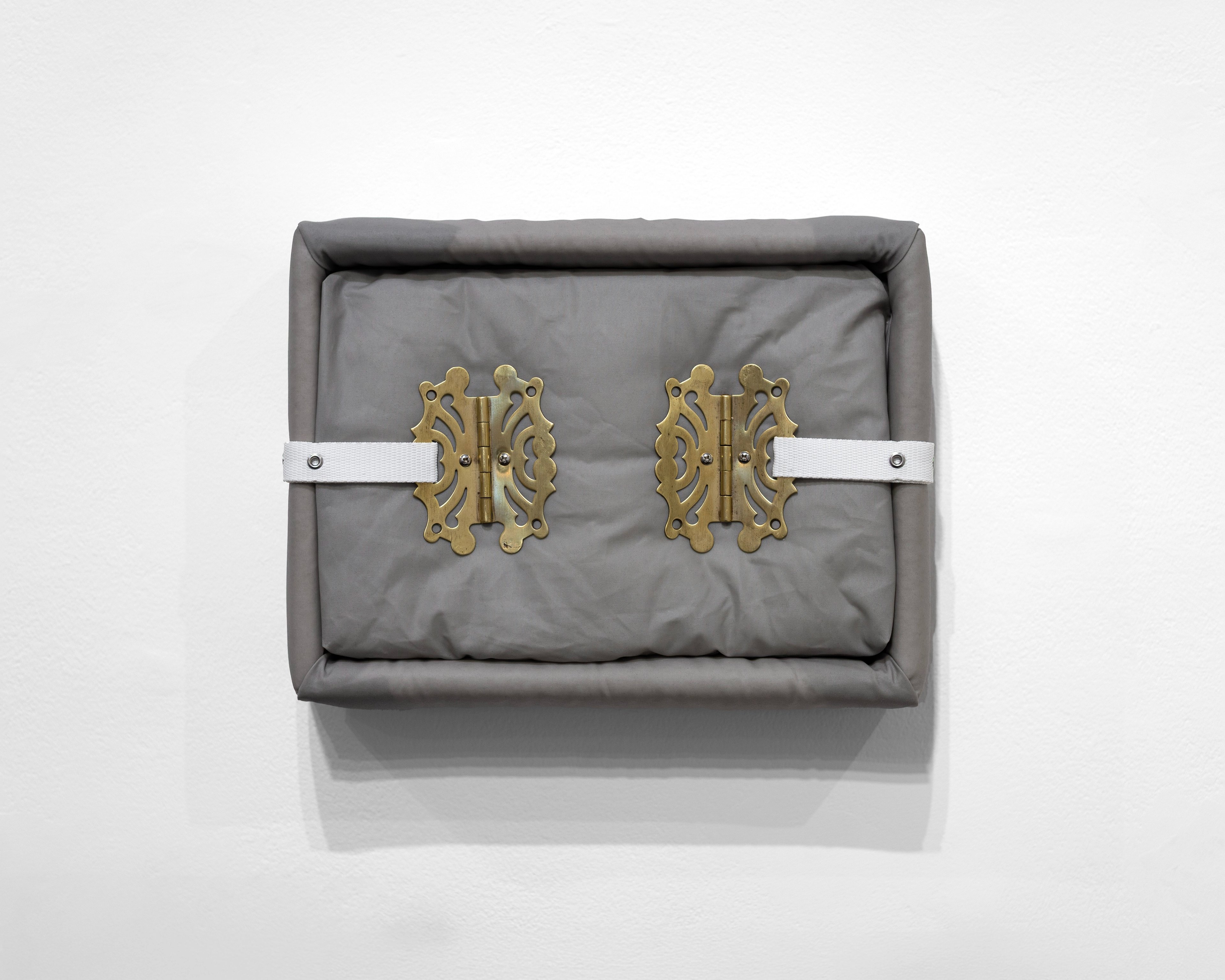 Gray oilskin box with quilted surface and ornate brass cabinet hinges secured by white metal straps, viewed from above