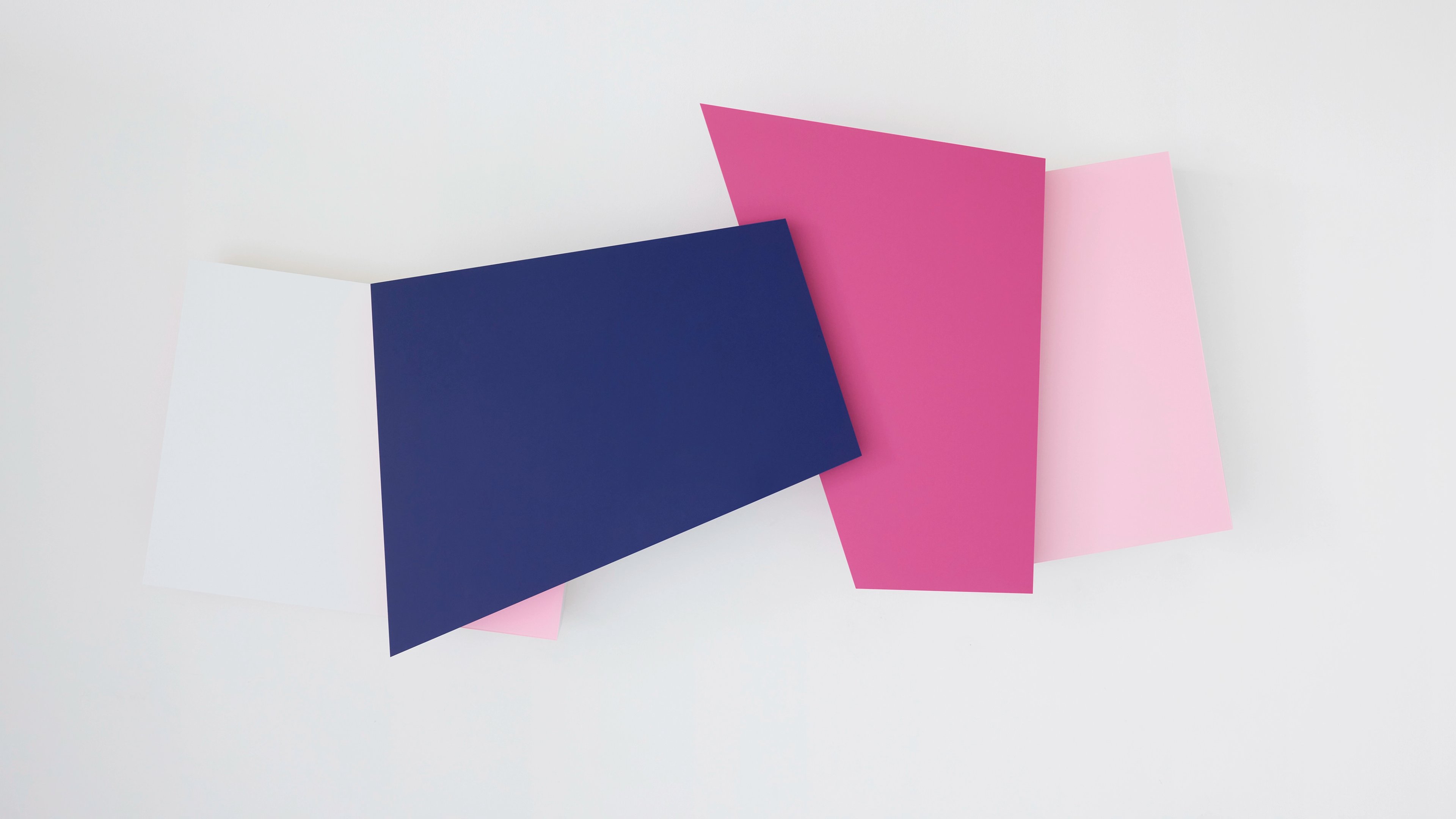 Three overlapping geometric panels in navy blue, hot pink, and pale pink arranged at angular intervals against a white wall.