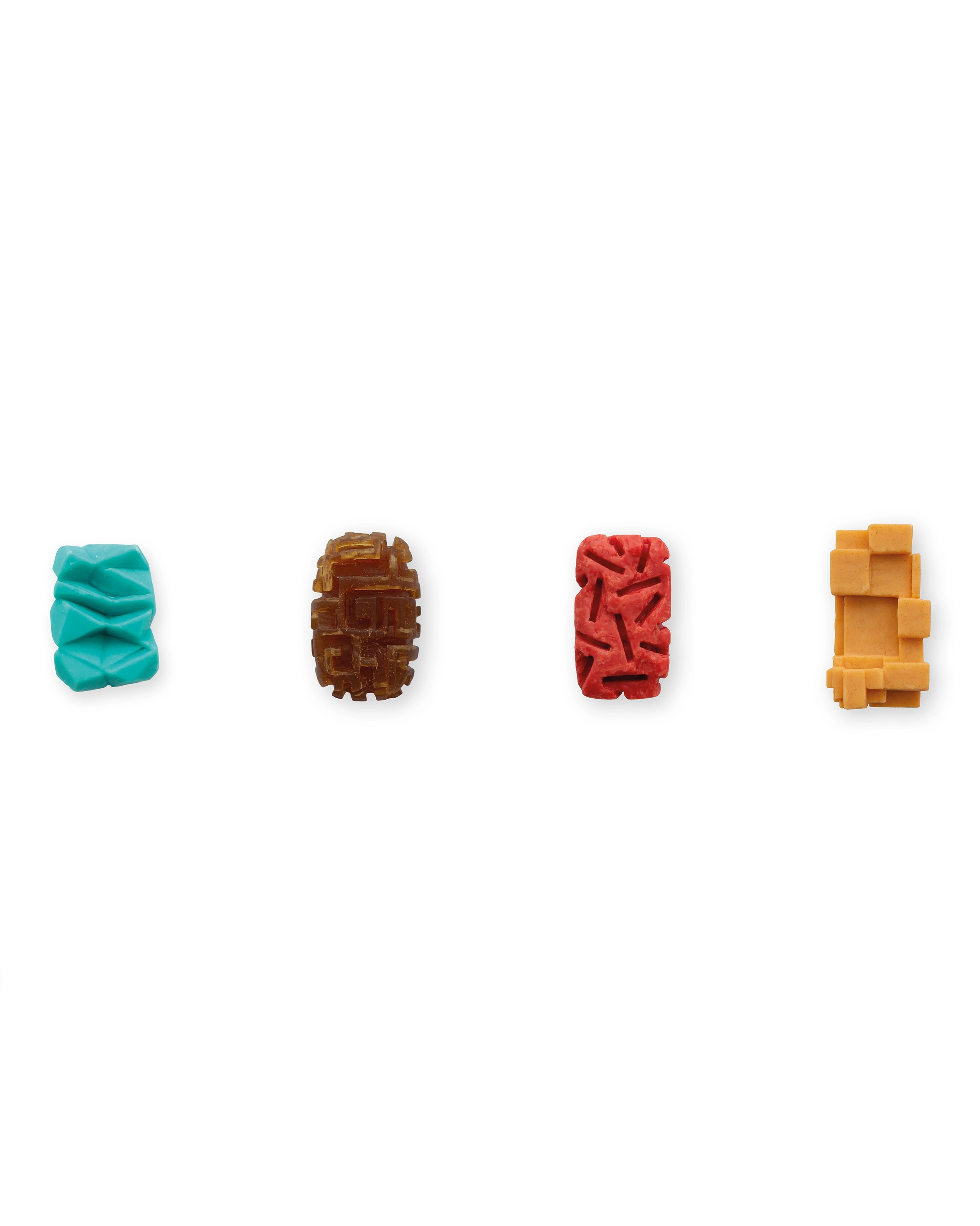 Four carved soap bars in turquoise, brown, red, and yellow arranged in a row, each with distinct textured and geometric surface patterns