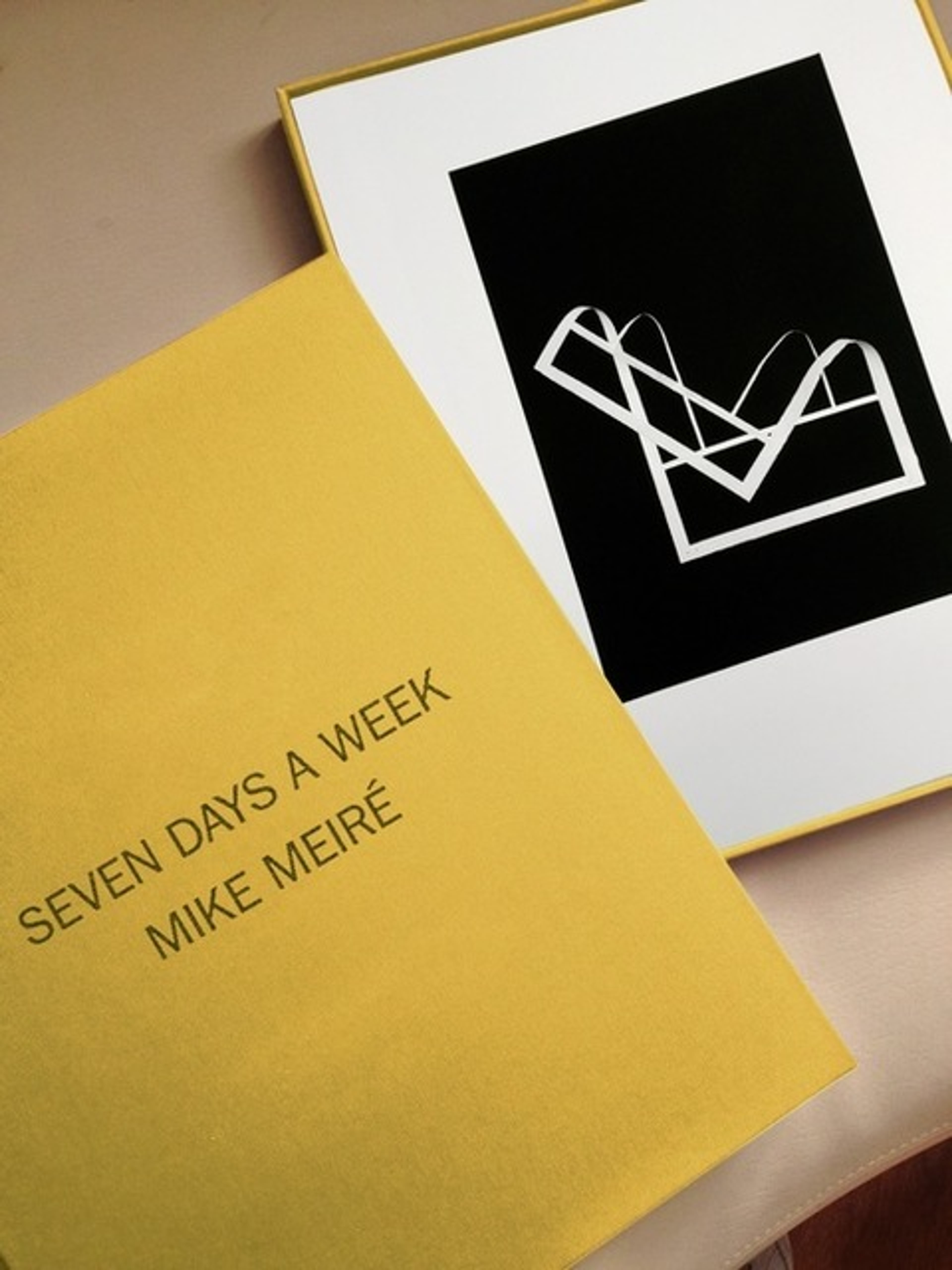 Two silkscreen prints in a gold-edged box: yellow cover with black text reading "SEVEN DAYS A WEEK MIKE MEIRÉ," and black sheet with white geometric line dra…