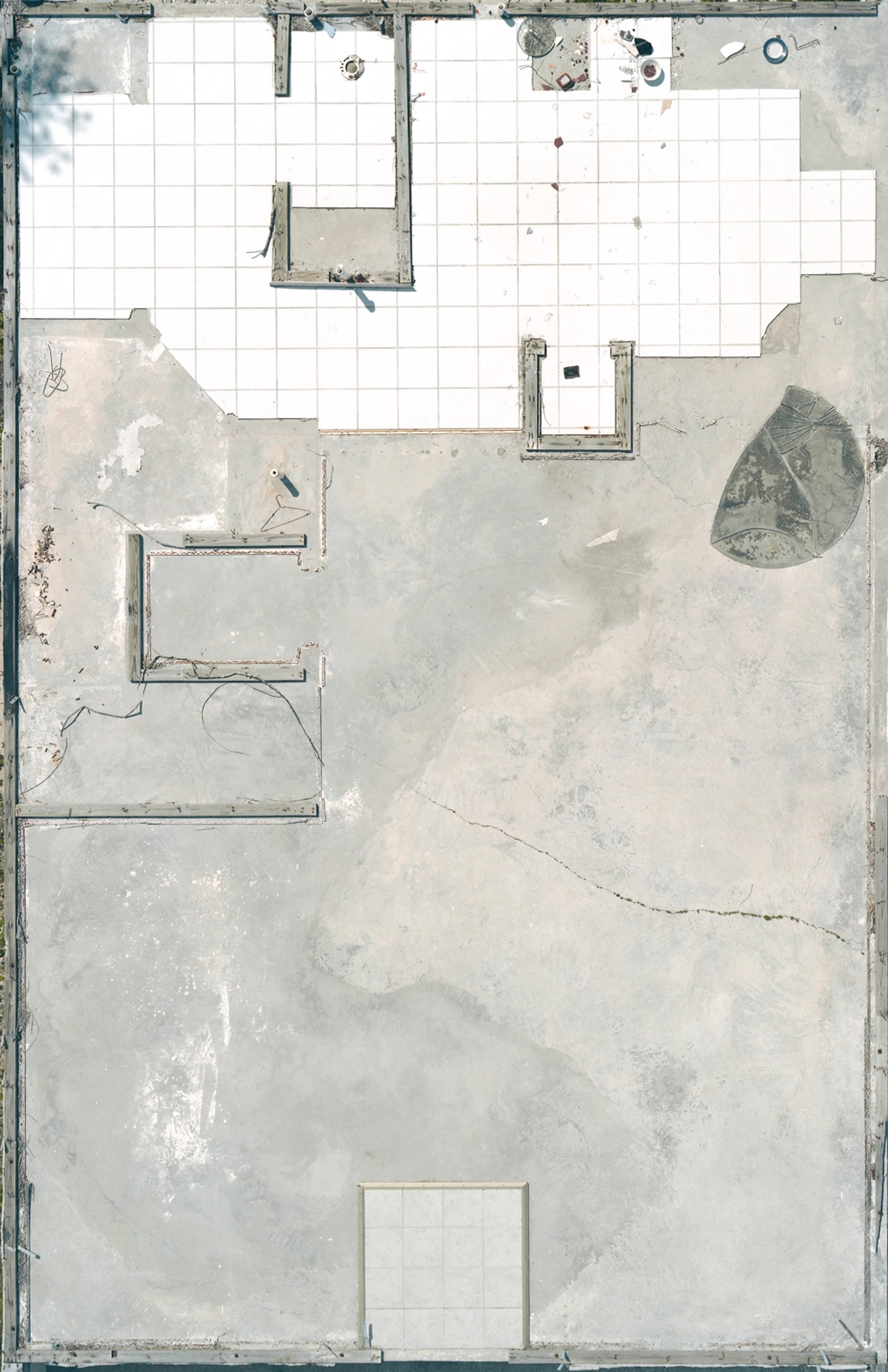 Overhead view of an abandoned building interior with white tile flooring, concrete walls, scattered debris, and architectural elements rendered in muted gray…