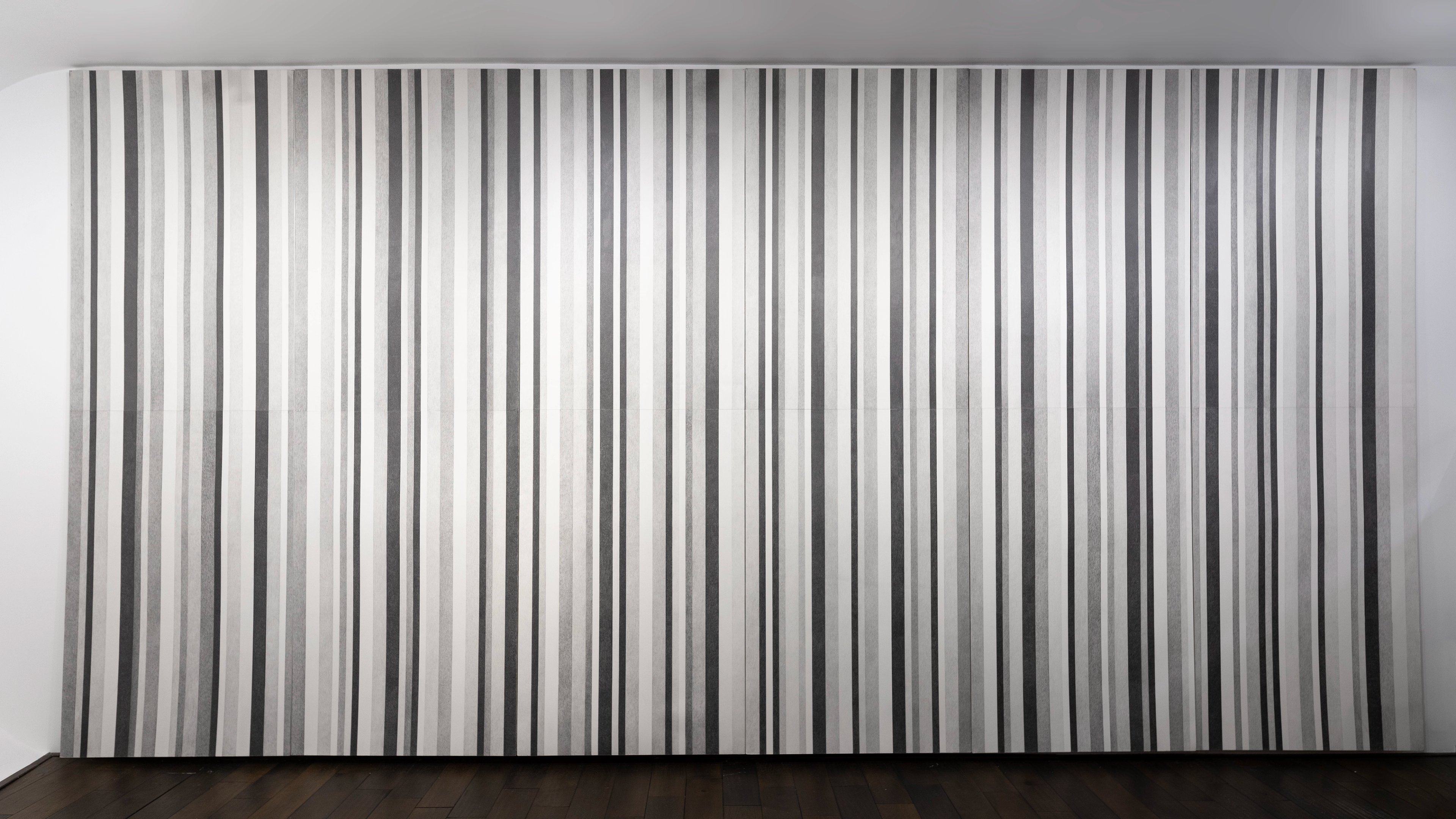Dense grid of vertical graphite lines in varying widths and tones creating an abstract striped wall installation in shades of grey and black.