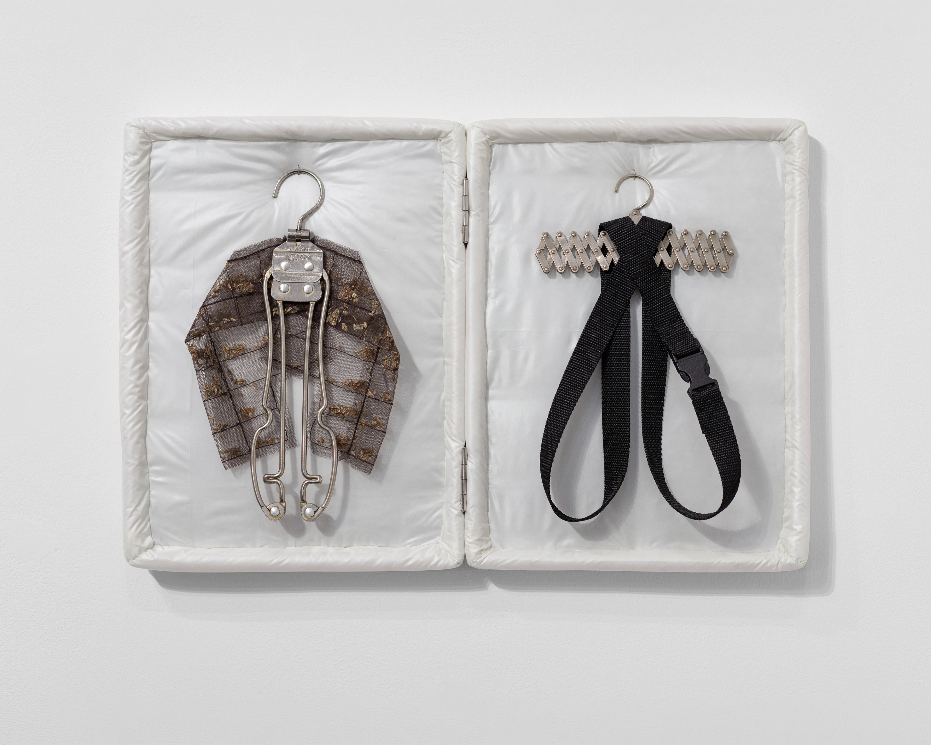 Two white-lined display cases containing metallic hangers: left holds a brown patterned fabric jacket; right displays a black webbing strap with metal hardwa…