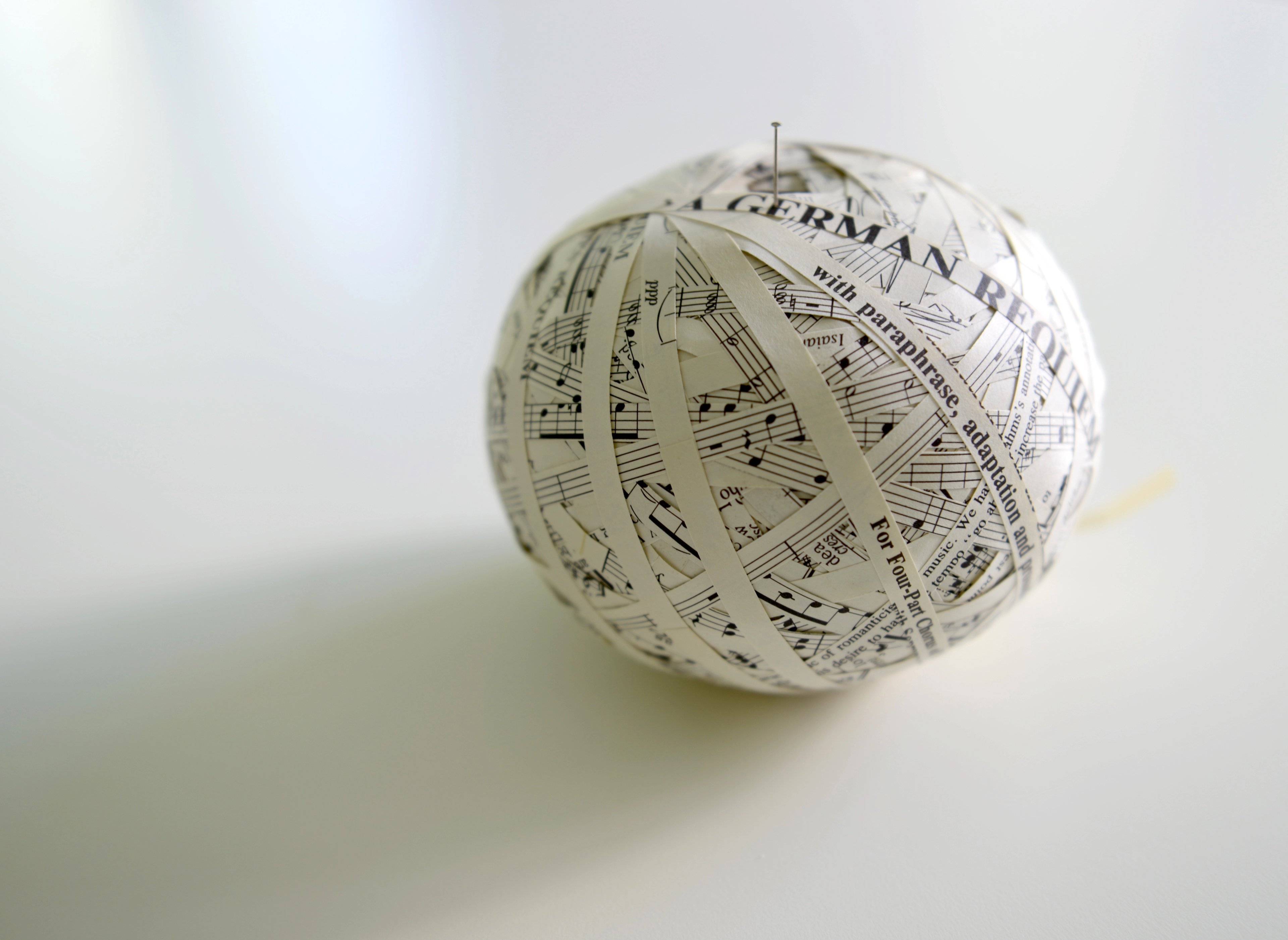 Spherical sculpture made from cut and folded paper printed with musical notation and text, suspended against a white background