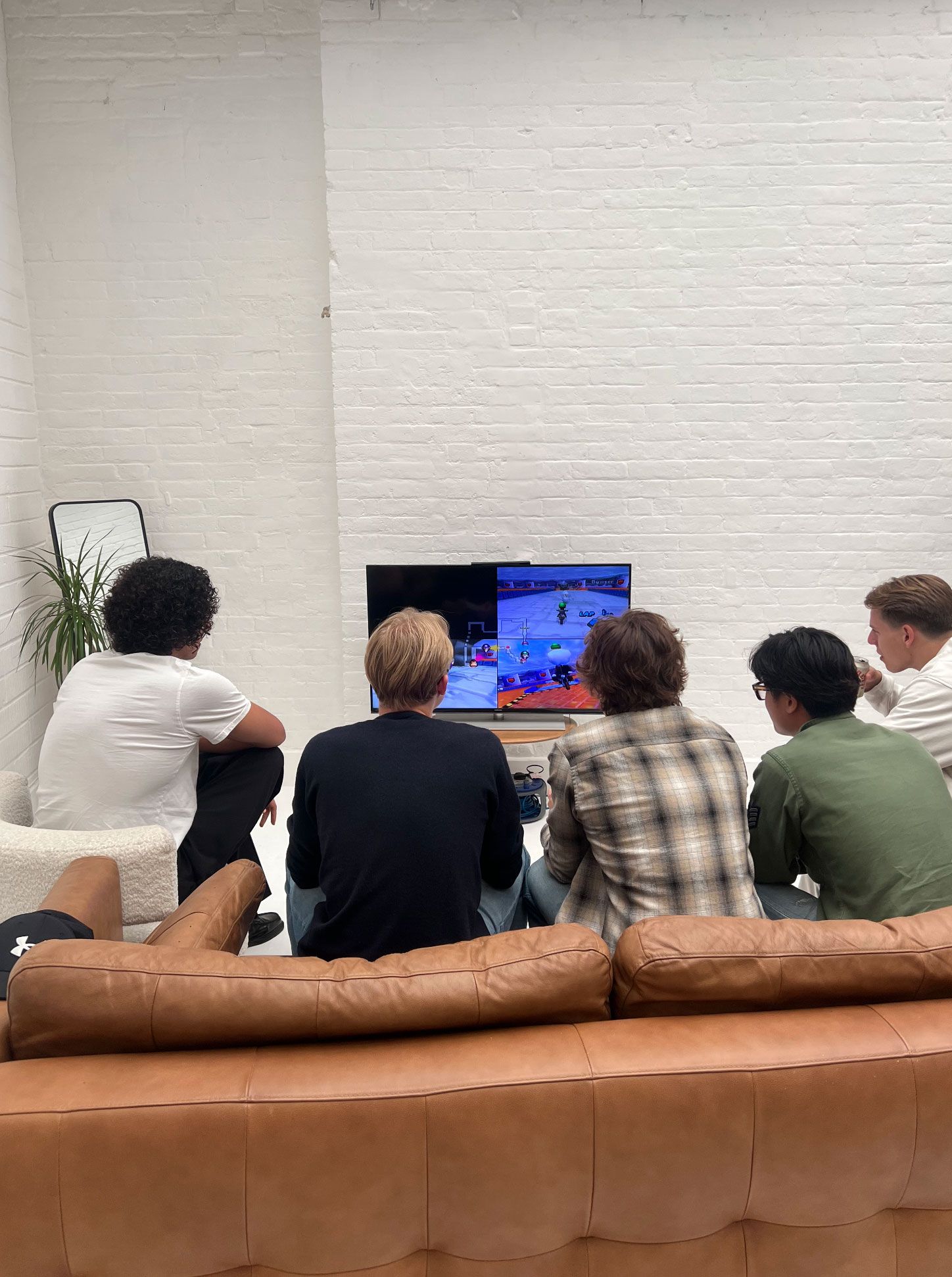 Group of guests sitting on leather sofas at Brixton Warehouse playing a video game together — part of a relaxed creative event in the studio’s lounge area.