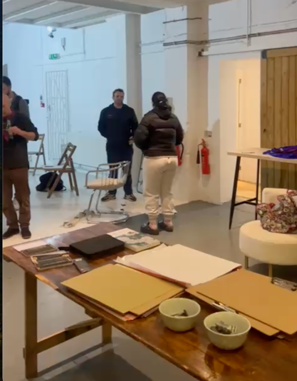 Heavily tattooed life model posing on a rug in a bright white studio at Brixton Warehouse, while an artist sketches during a life drawing class.