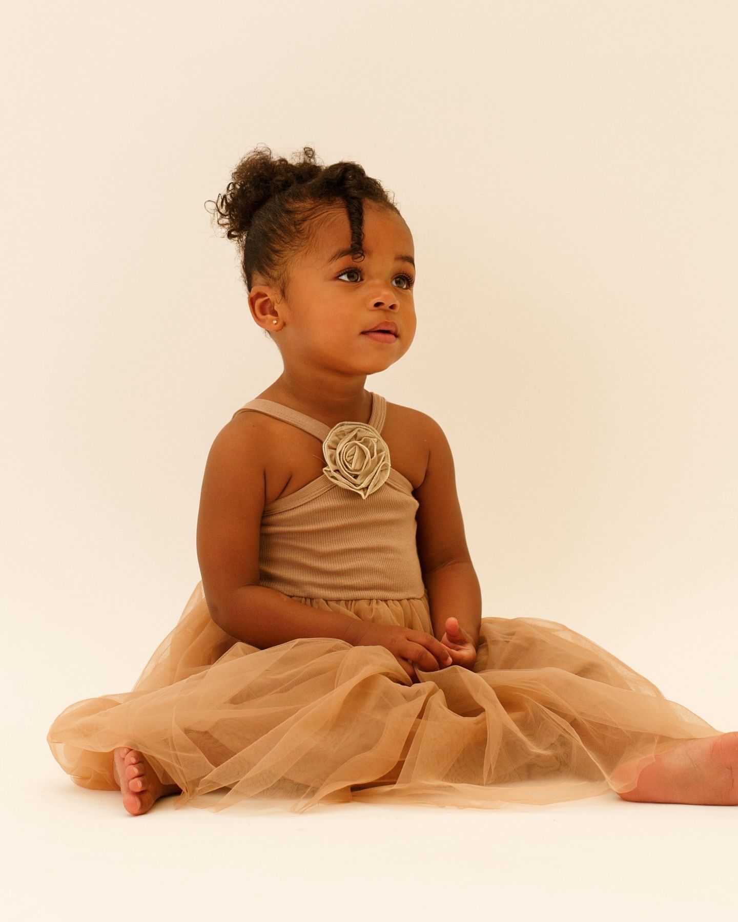 Cute baby or toddler model wearing a pale cream party dress with a ribbed vest top, fabric flower detail, and a netting skirt.