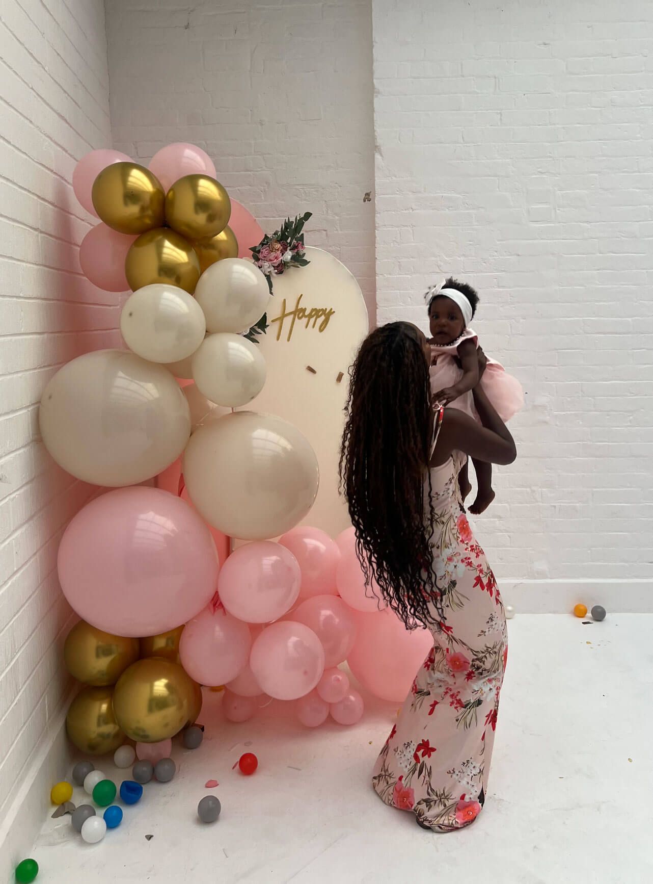 “Mother lifting baby during a baby shower at Brixton Warehouse, with pink and gold balloon decorations.”
