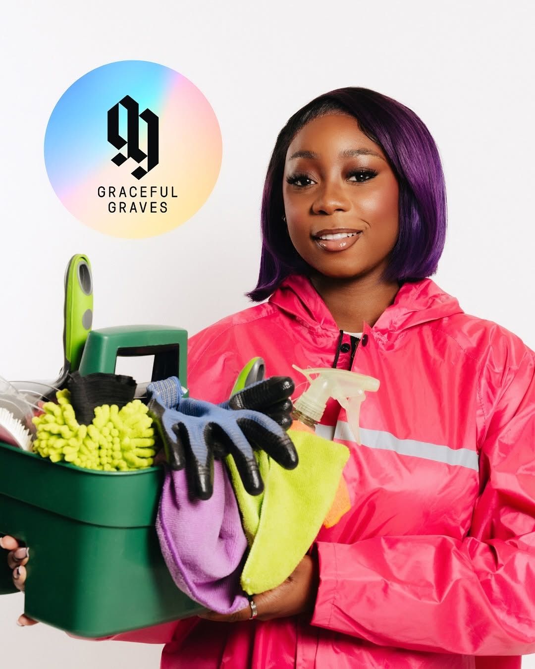 Graceful Graves founder holding cleaning supplies during a brand photoshoot, wearing a pink jacket against a clean studio background.