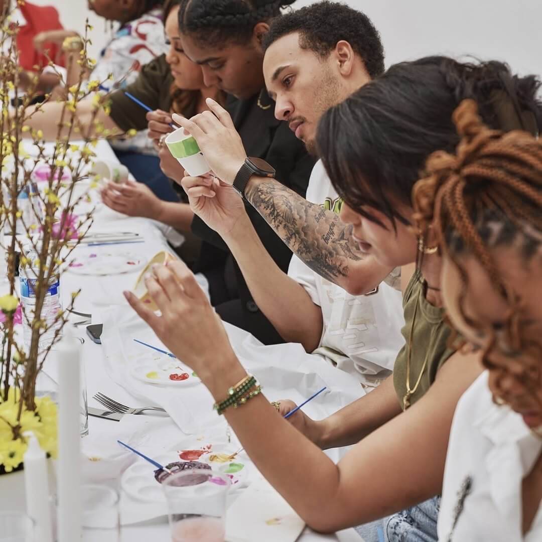 “Guests at Brixton Warehouse taking part in a sip and paint event, enjoying creative activities around a communal dining table.”