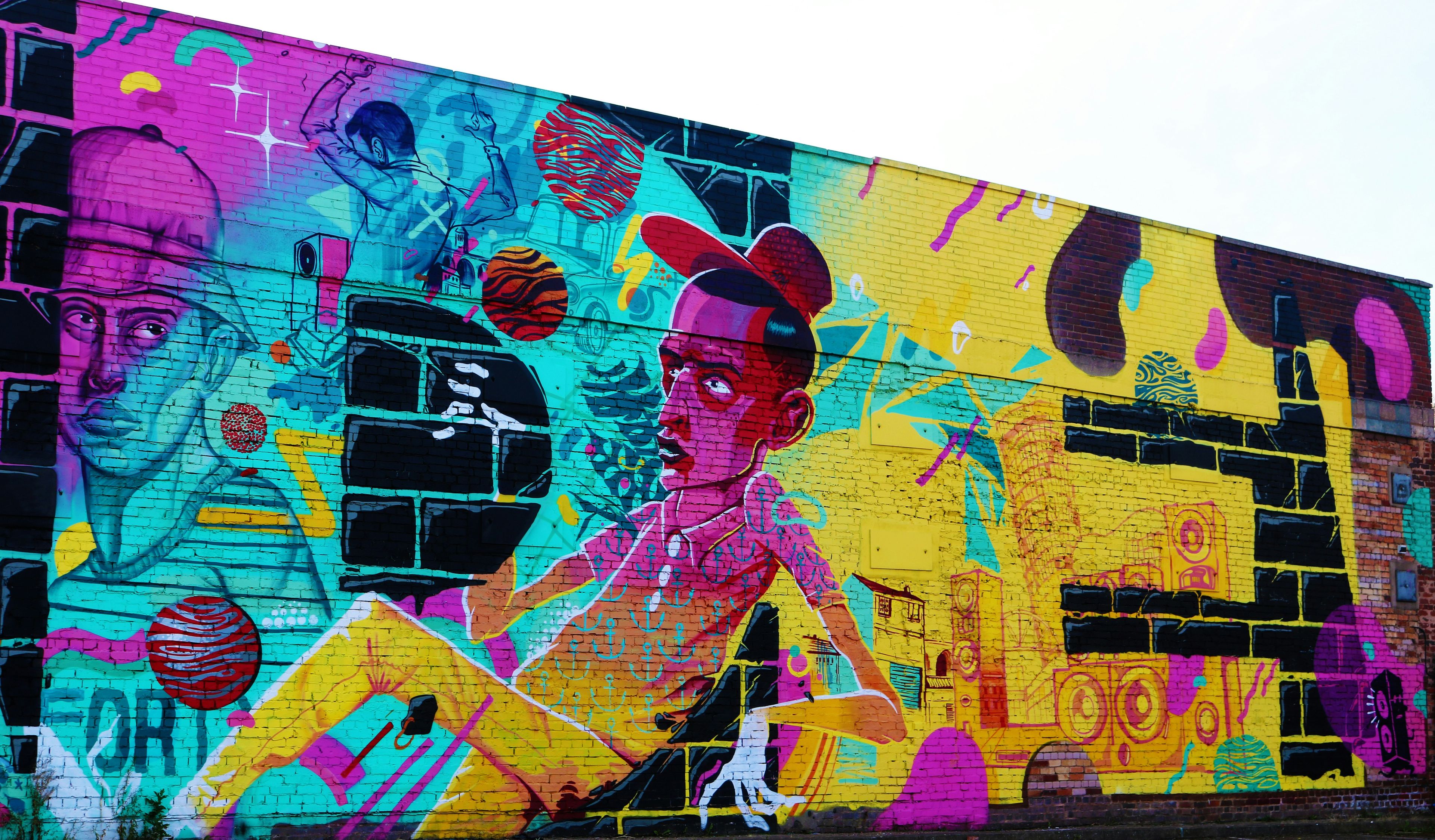 Large colourful street art mural on a brick wall in Digbeth, Birmingham, with cyan, magenta, and yellow graffiti