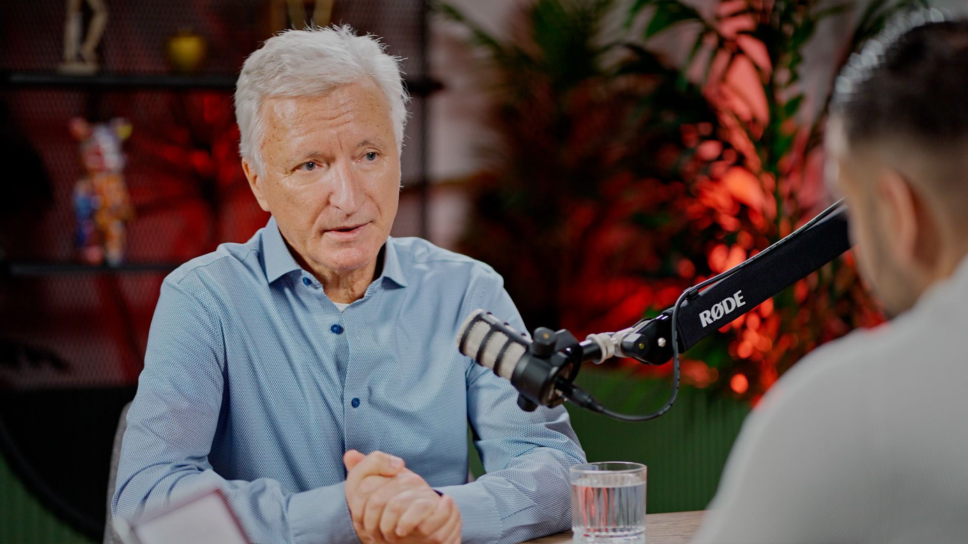 Senior podcast guest in a blue shirt speaking with the host in the Spotware studio.