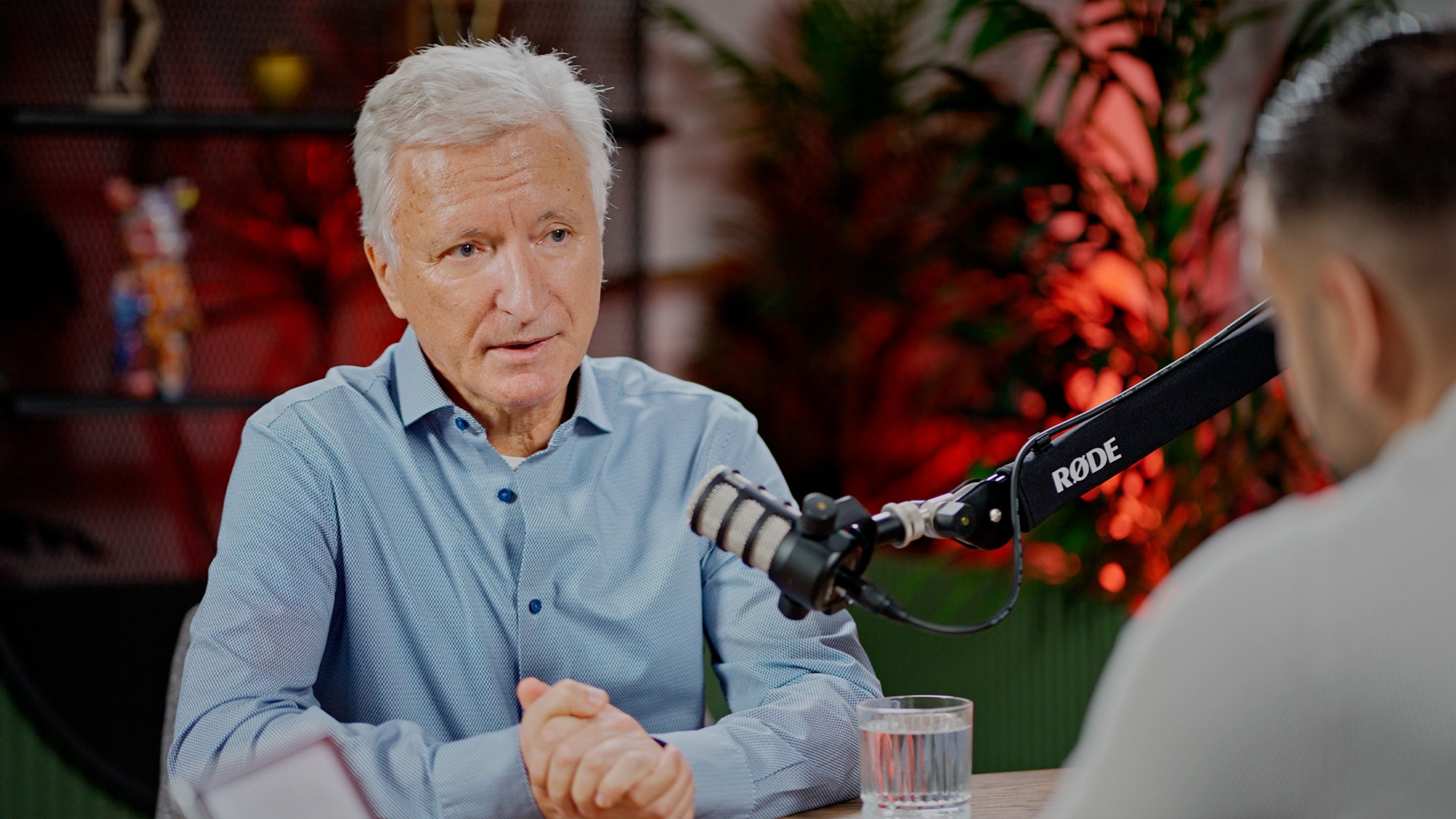 Senior podcast guest in a blue shirt speaking with the host in the Spotware studio.