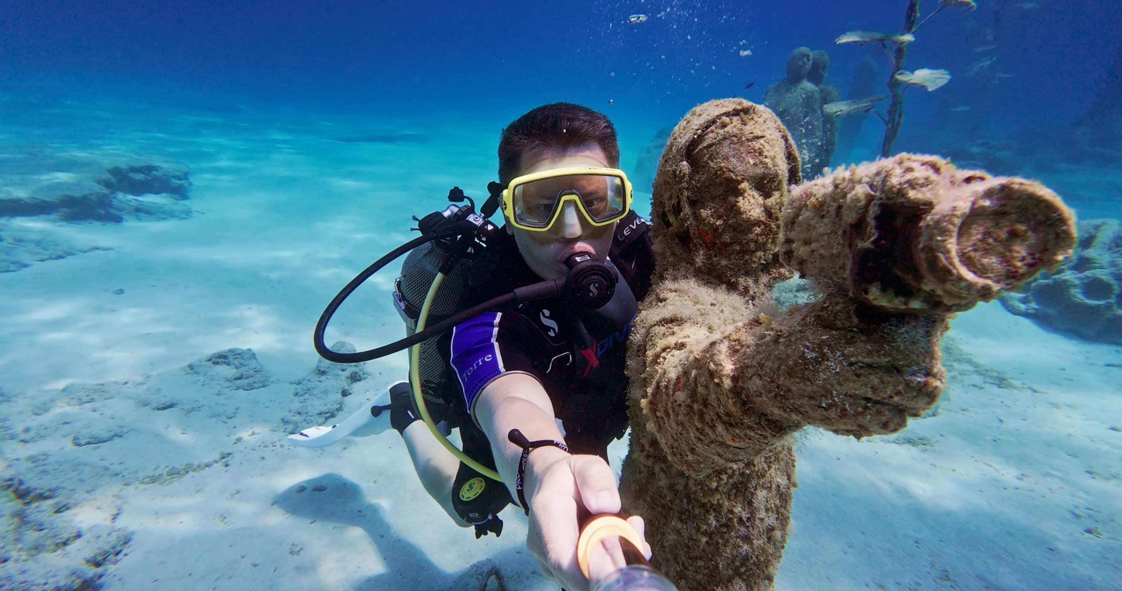 Scuba diver filming beside an underwater statue in the clear sea around Cyprus.