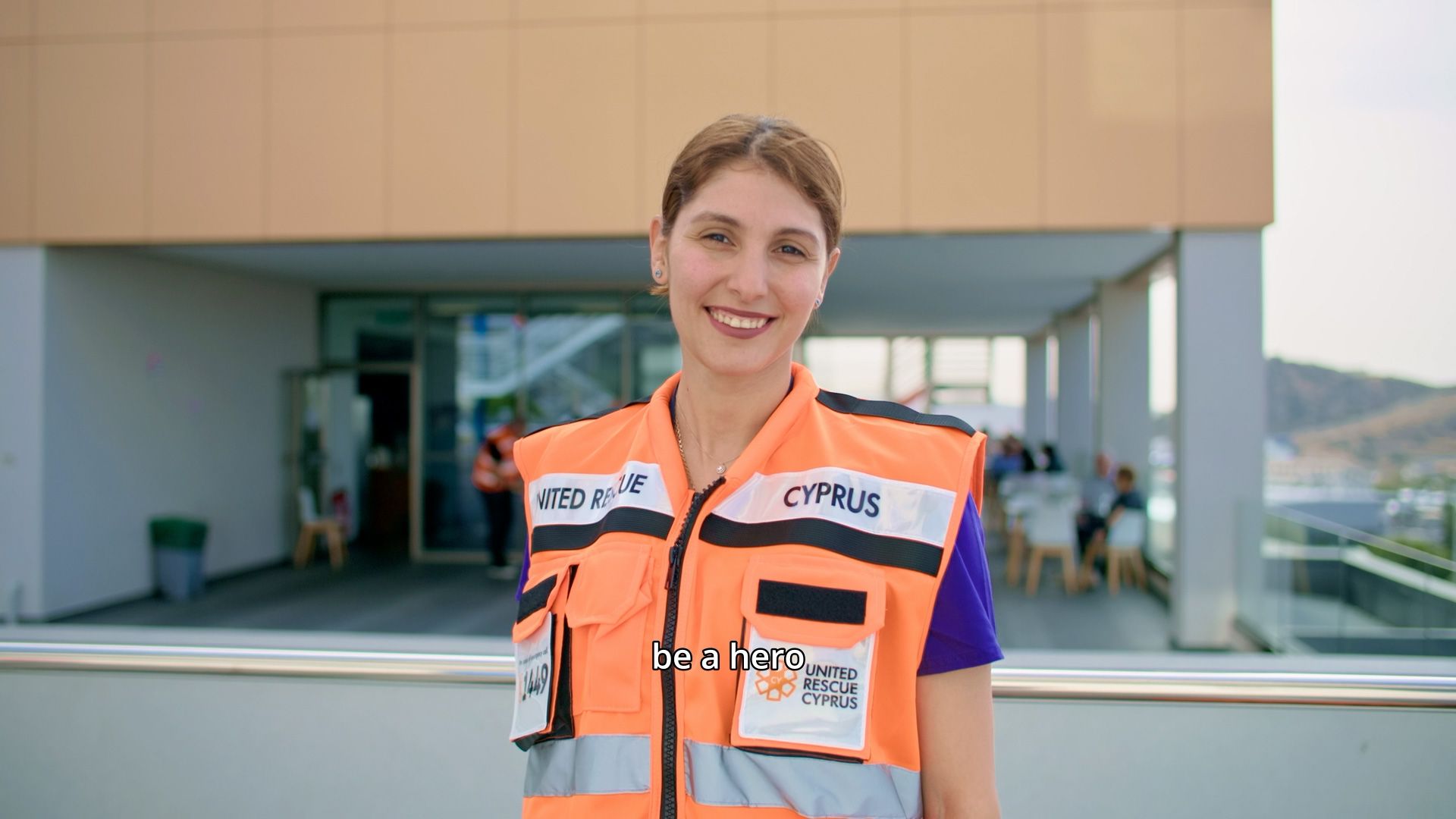 Young United Rescue Cyprus volunteer smiling in an orange emergency vest.