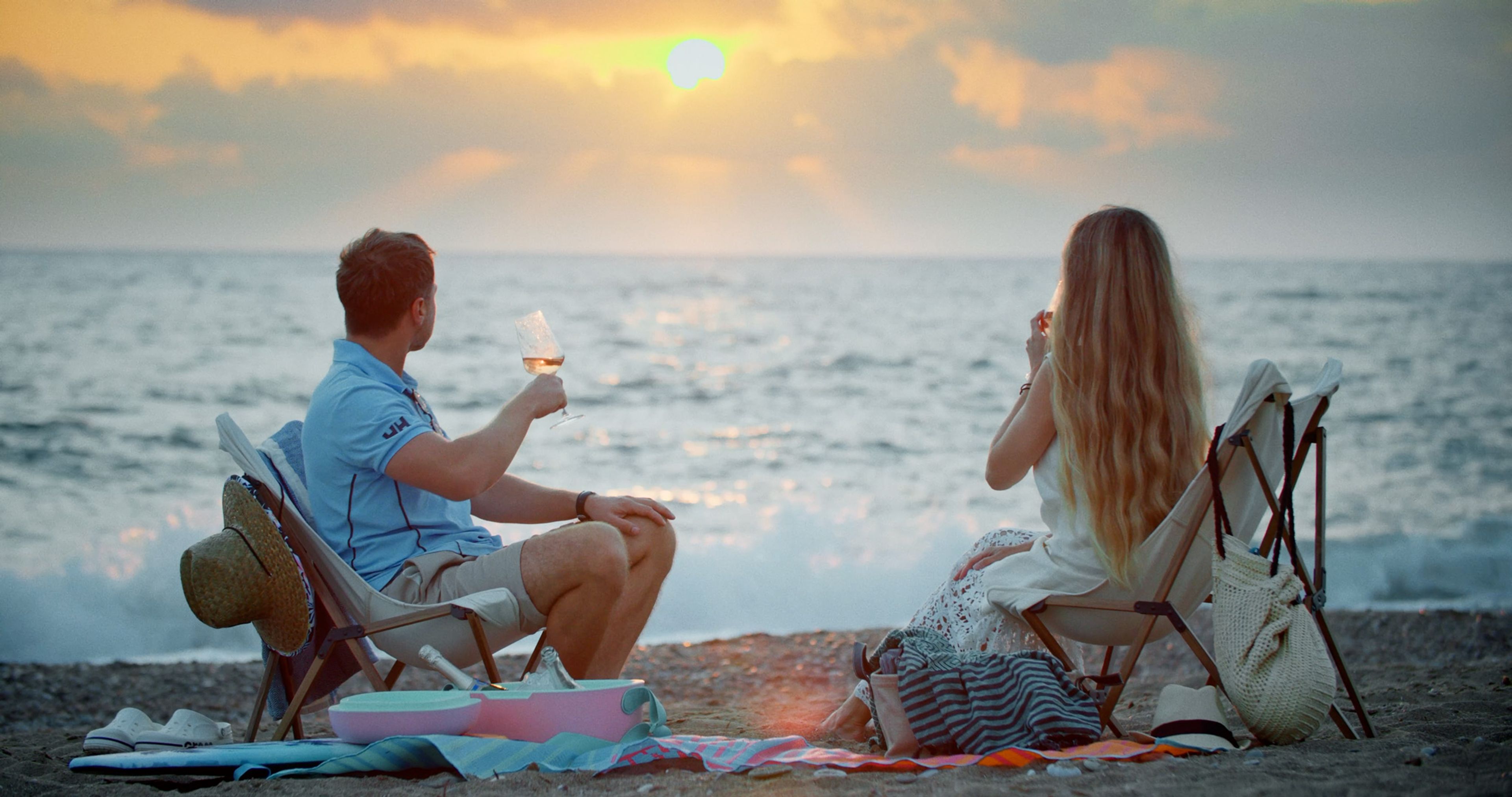 A young couple sitting by the sea with glasses of wine at sunset.