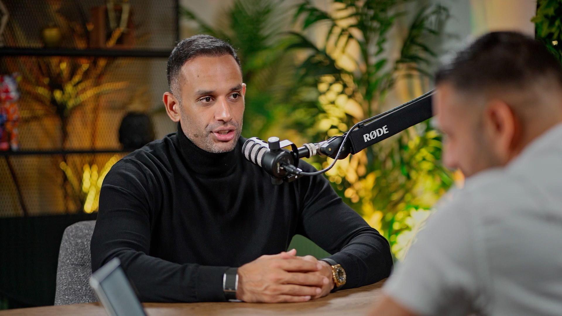Podcast guest in a black turtleneck speaking into a professional studio microphone.