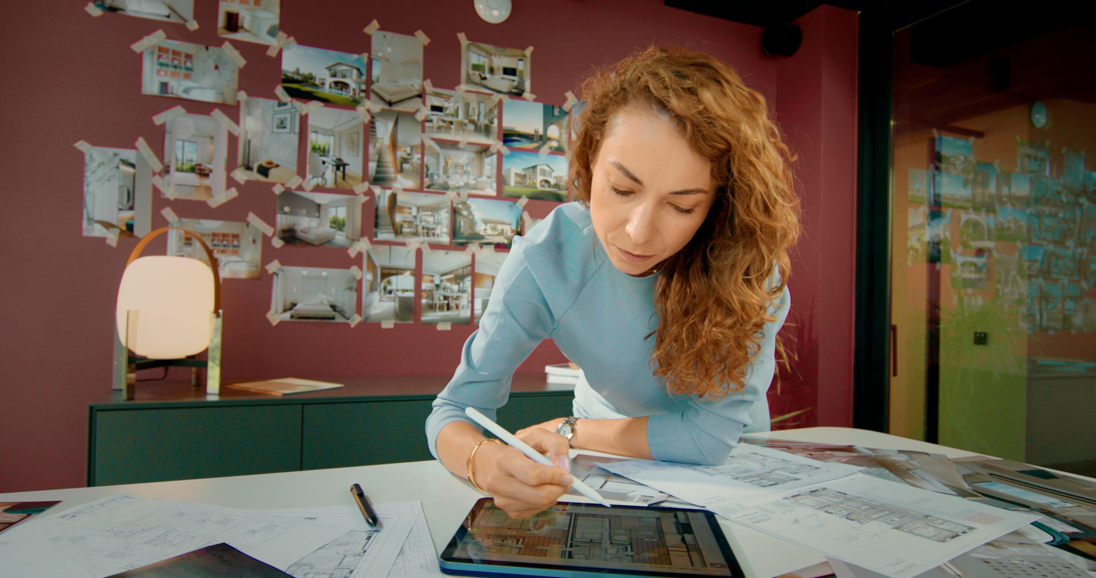 Nataly Bolshakova drawing on a tablet beside plans and architectural references