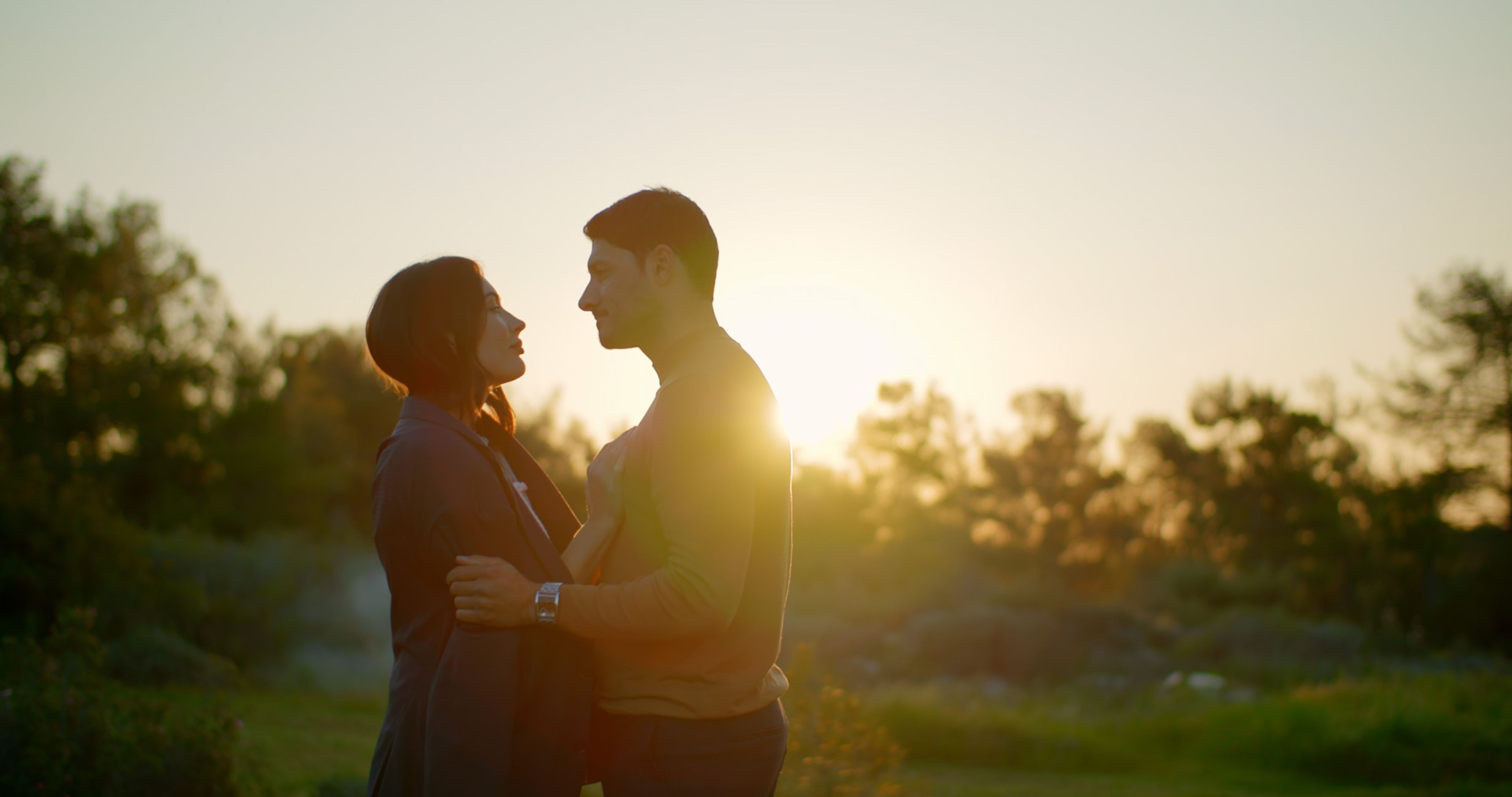 Couple standing together among trees at sunset