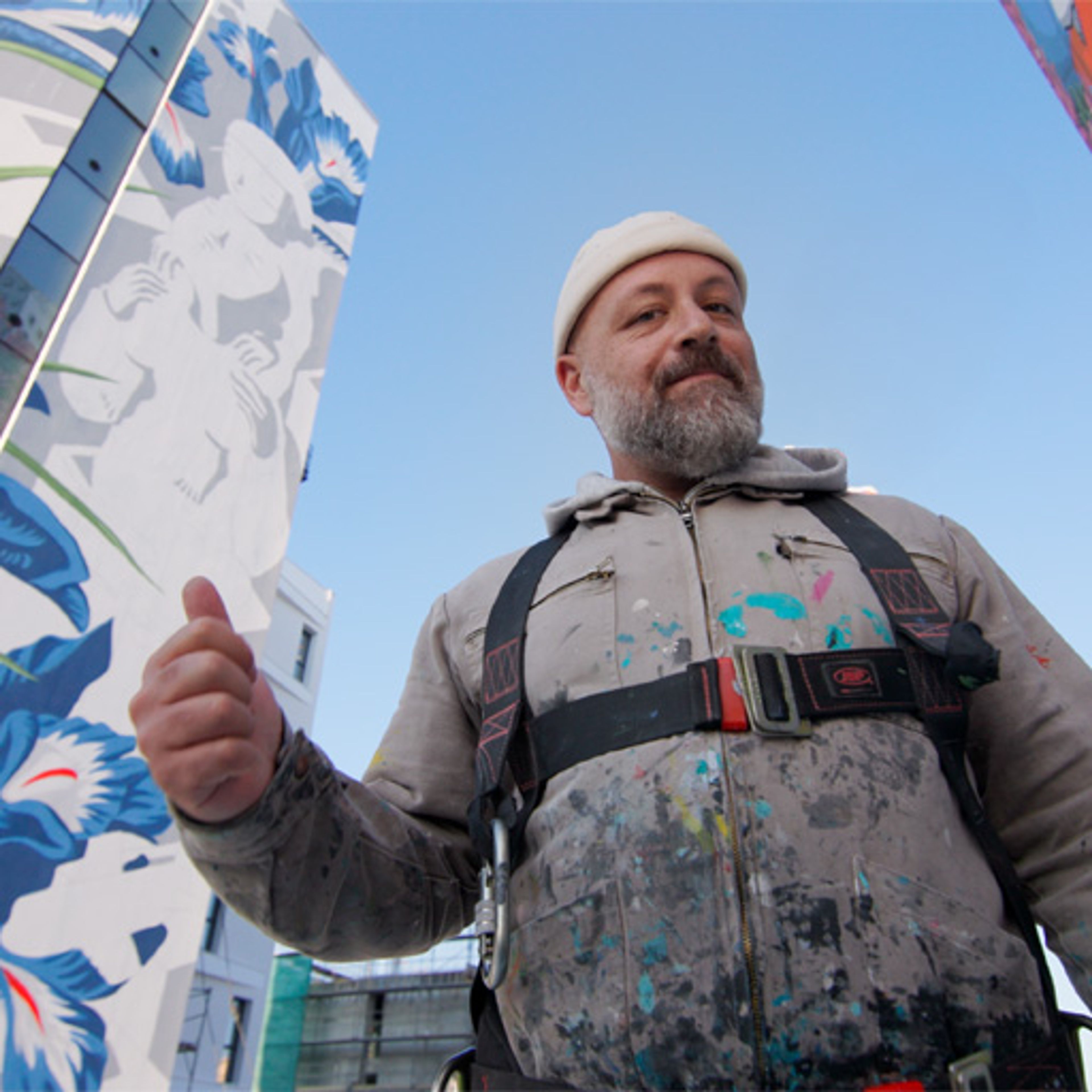 Italian artist Millo standing between the large-scale murals at Art Square in Limassol.
