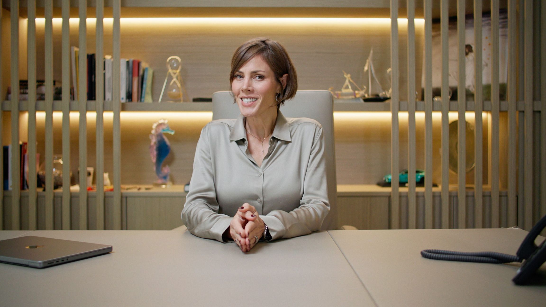 Female presenter speaking from a desk inside a modern bbf: office.