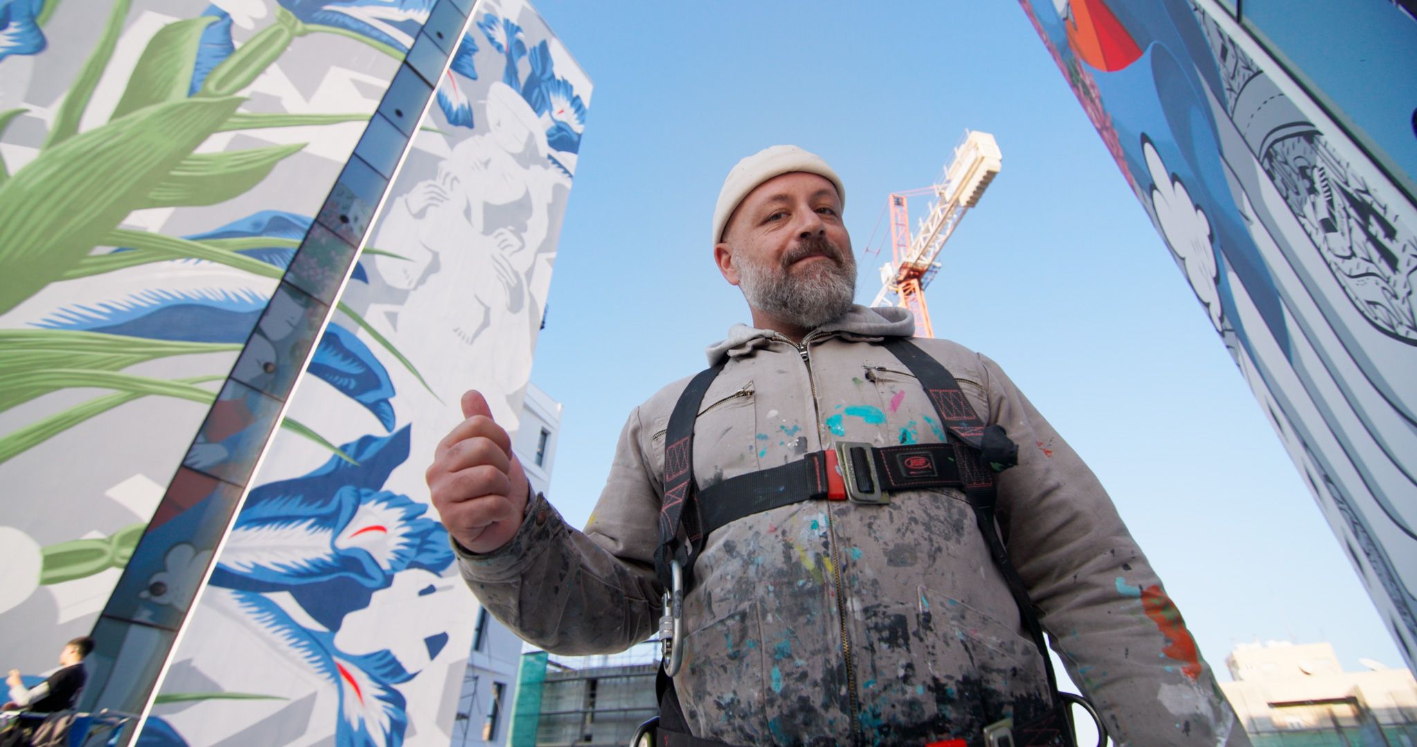 Italian artist Millo standing between two completed murals at Art Square.