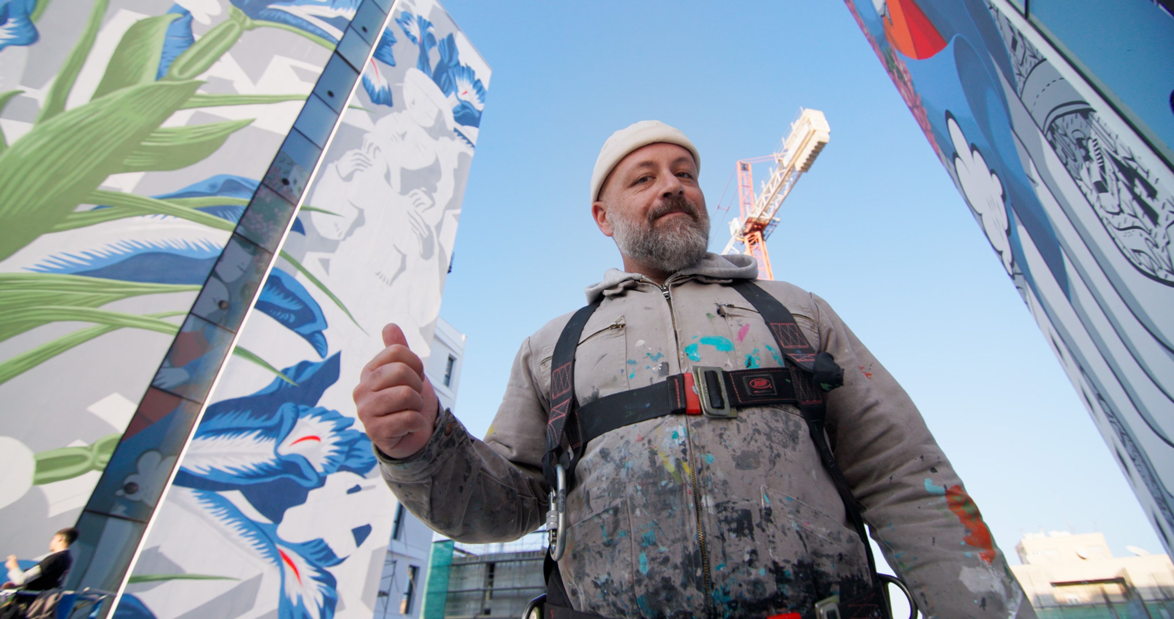 Italian artist Millo standing between two completed murals at Art Square.